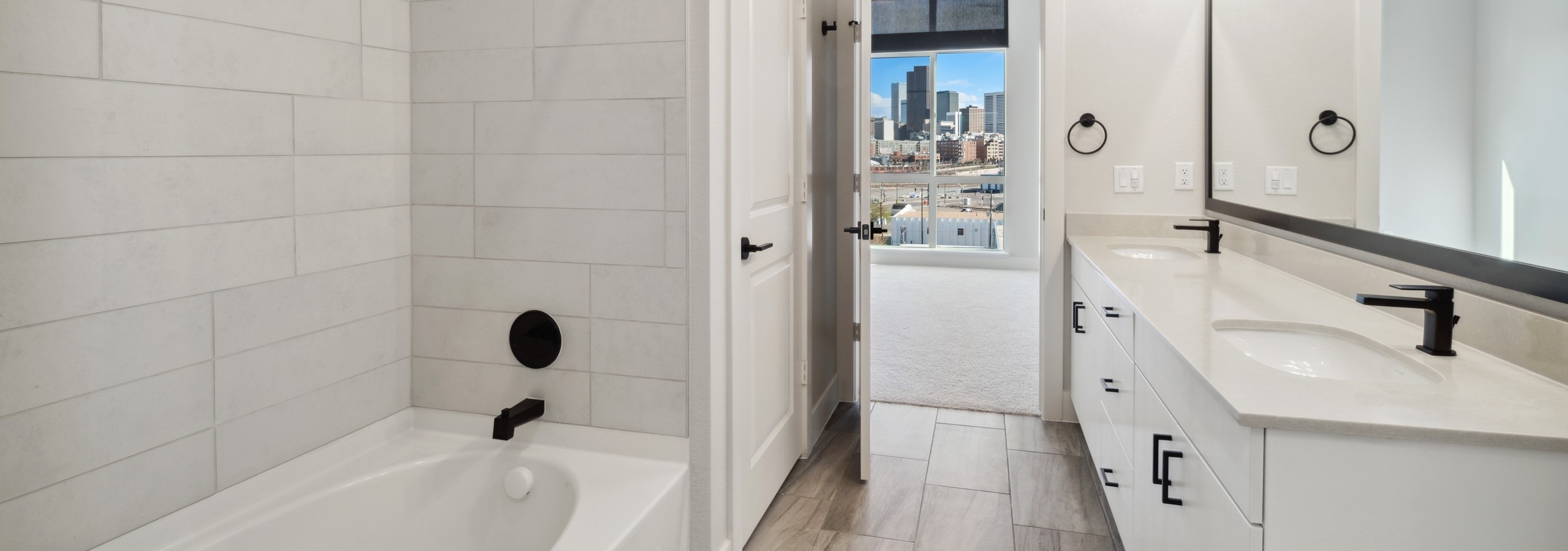 AMLI RiNo bathroom with white garden tub and tile surround and white cabinets and countertops and black finish hardware