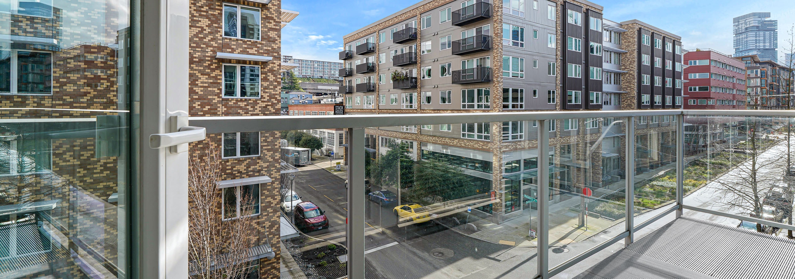 A large apartment balcony at AMLI 535 with glass door with views of South Lake Union with cars on the street and blue sky