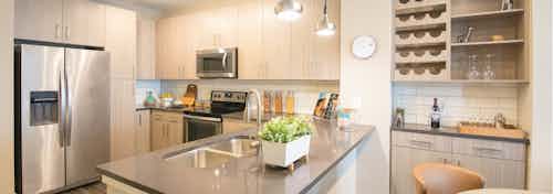 A kitchen at AMLI Dry Creek apartments with a granite counter top island and stainless steel appliances and overhead lighting
