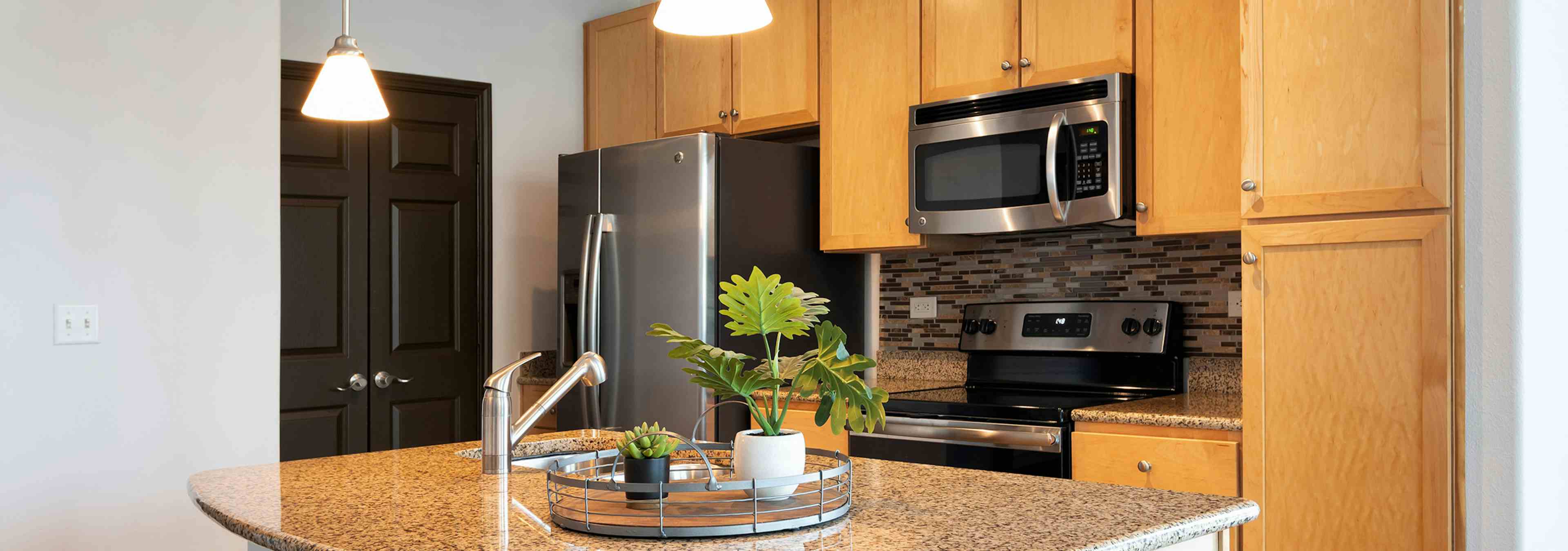 Interior view of AMLI 300 apartment kitchen with an island, custom wood cabinetry and stainless steel appliances