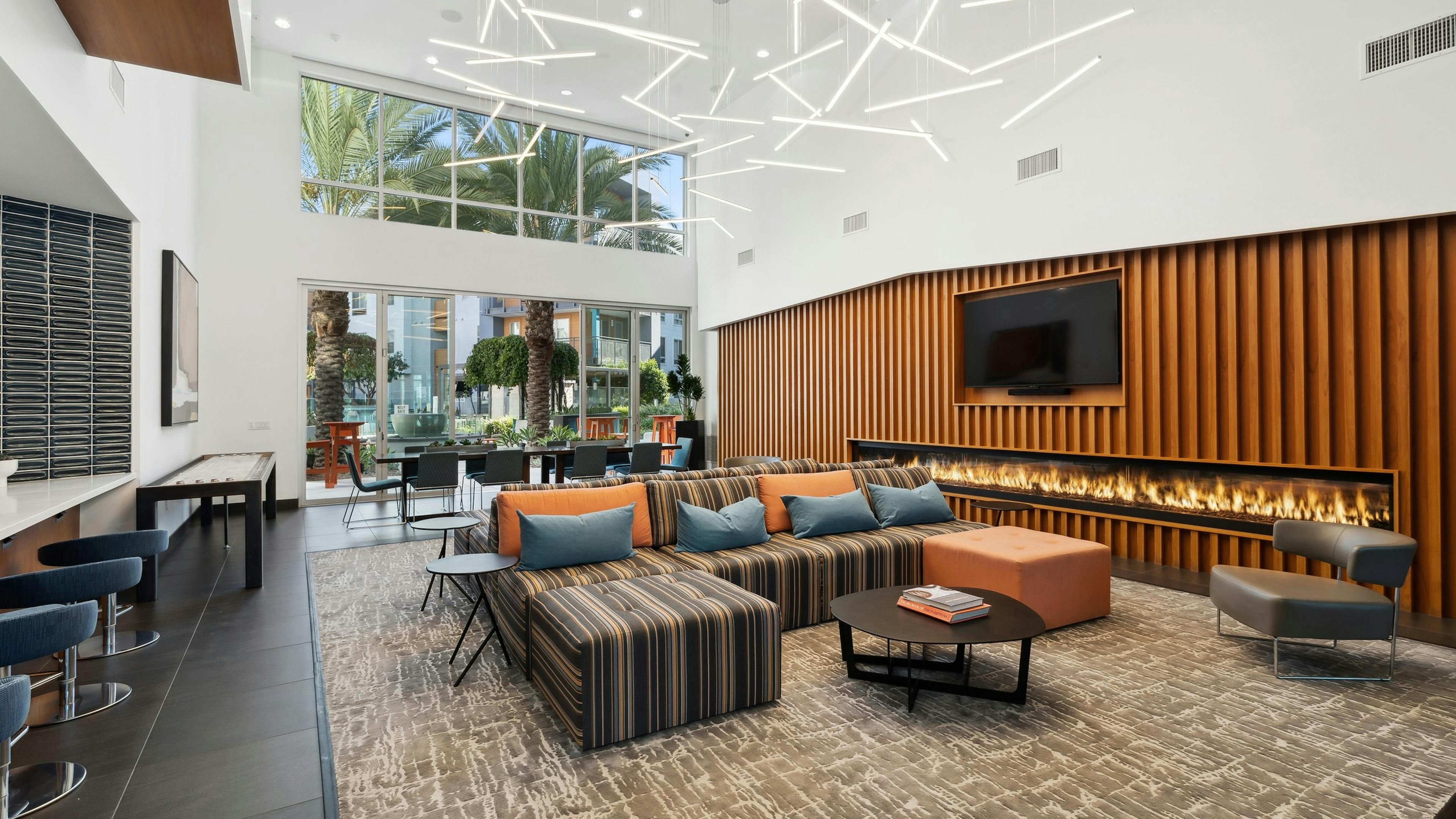 Interior view of clubroom at AMLI Uptown Orange apartments with long lit fireplace and brown couches and other seating