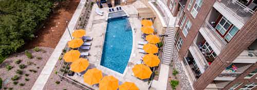 Ariel view of the pool area at AMLI Dry Creek apartments with several umbrellas and chairs with view of apartment balconies