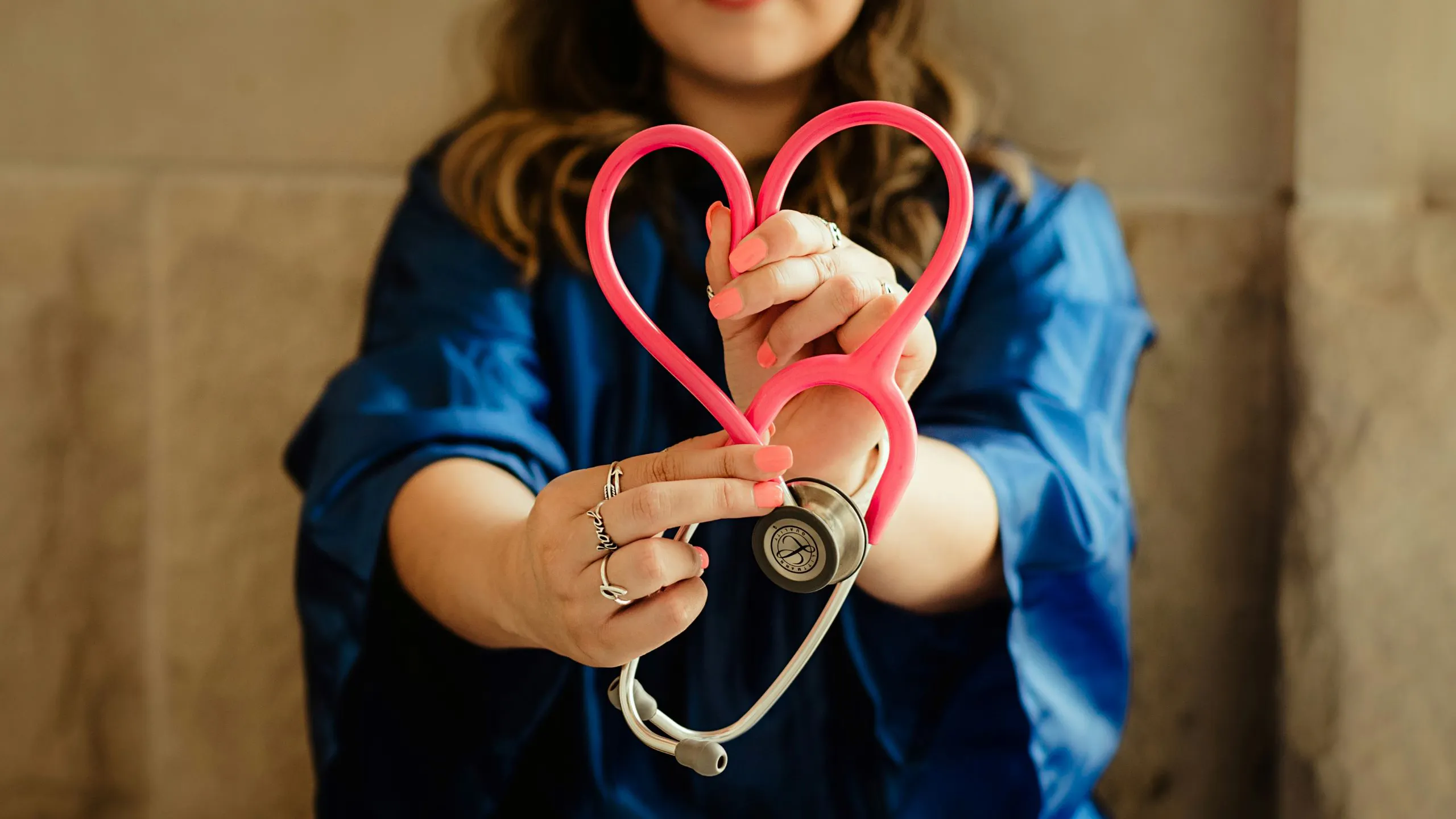 Woman in blue scrubs holding a pink stethoscope shaped like a heart
