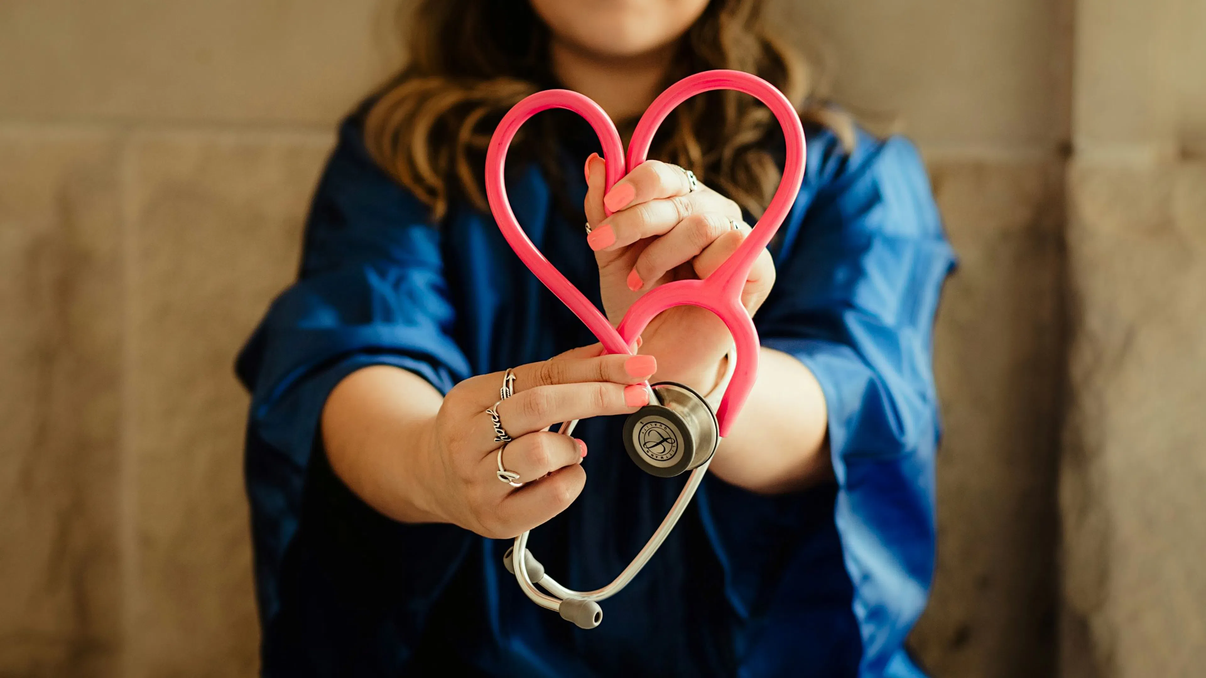 Woman in blue scrubs holding a pink stethoscope shaped like a heart