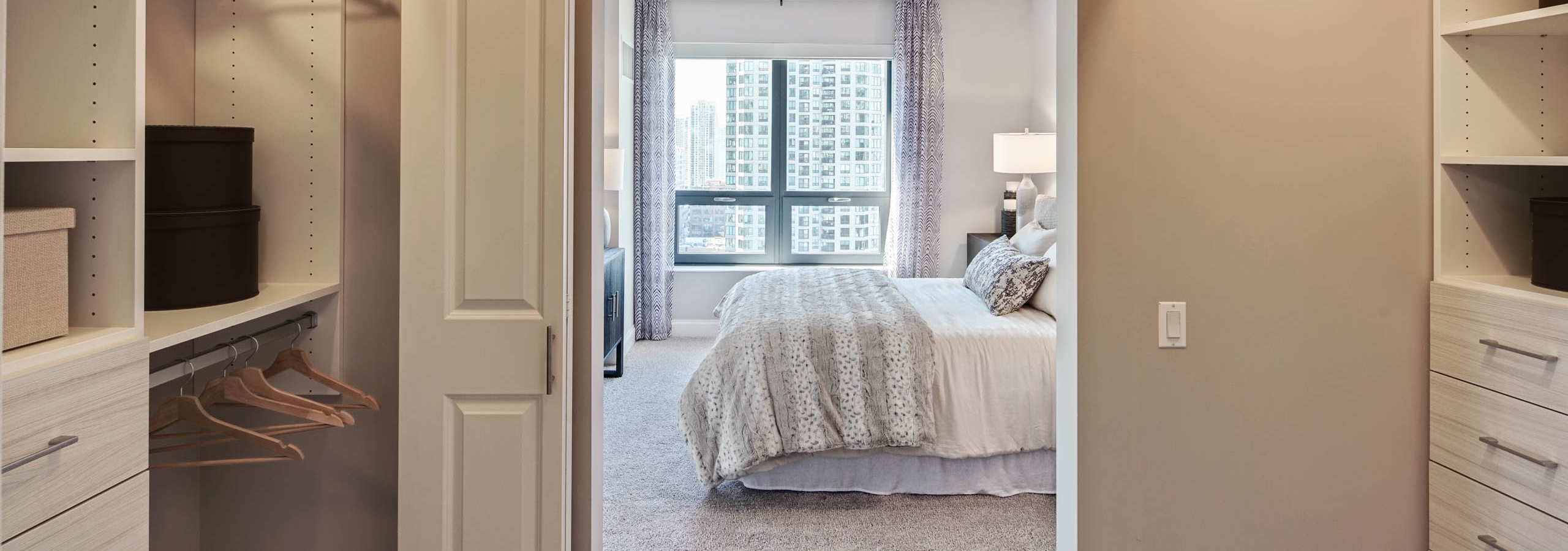 View of elegant AMLI River North apartment bedroom from luxurious walk in closet with ample space and built in shelving