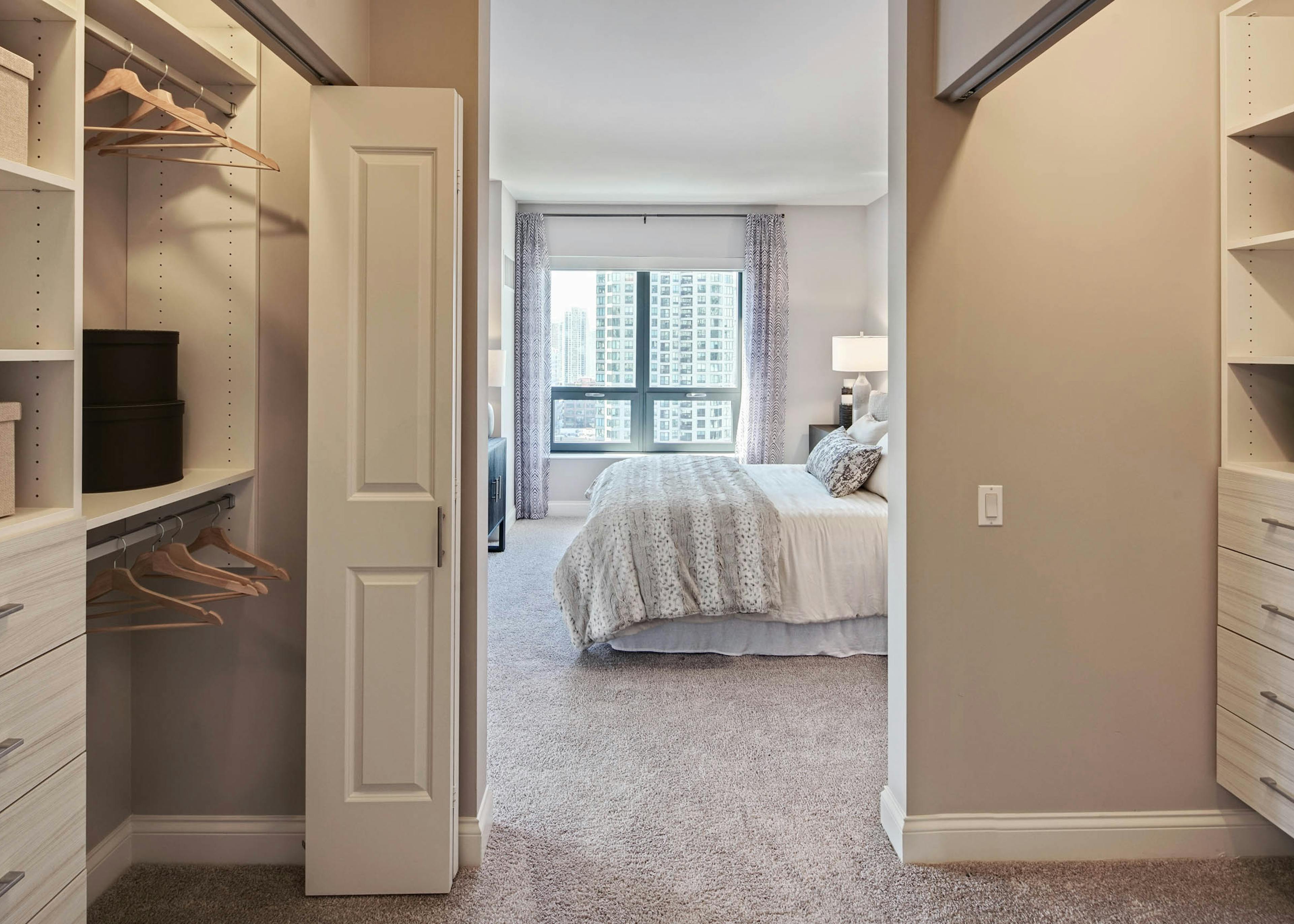 View of elegant AMLI River North apartment bedroom from luxurious walk in closet with ample space and built in shelving 