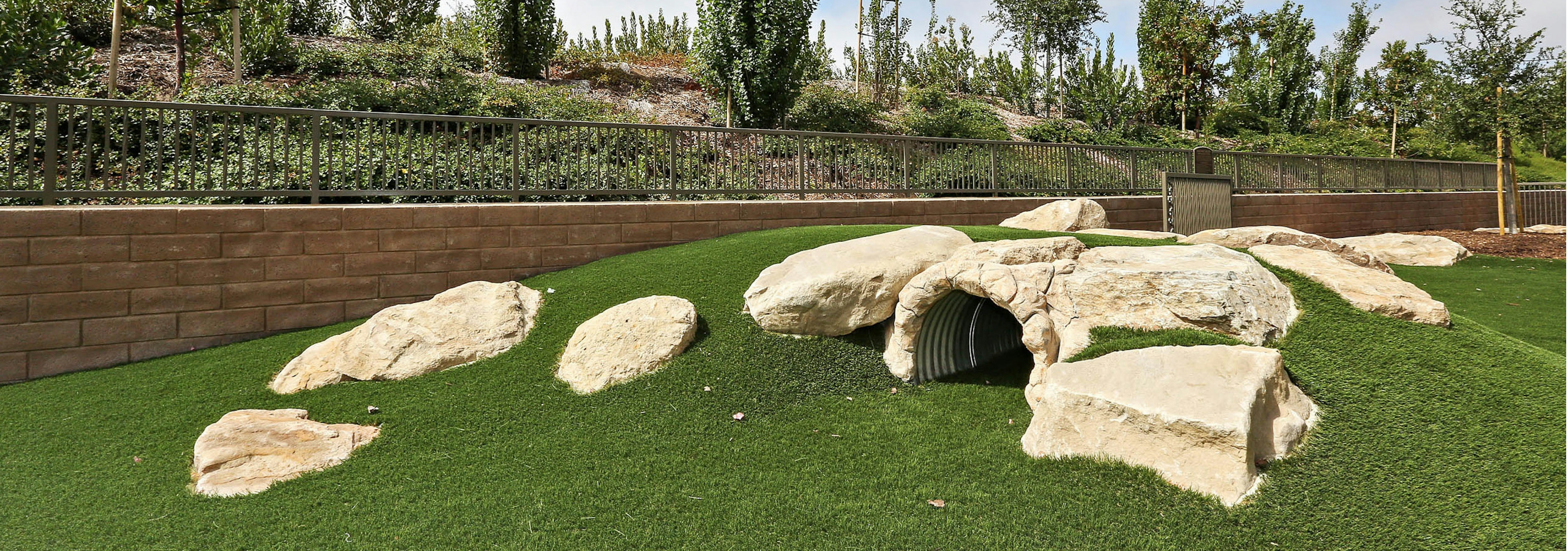 Close-up of pet park bark log tunnel on artificial pet turf hill and faux rocks at AMLI Spanish Hills apartment building