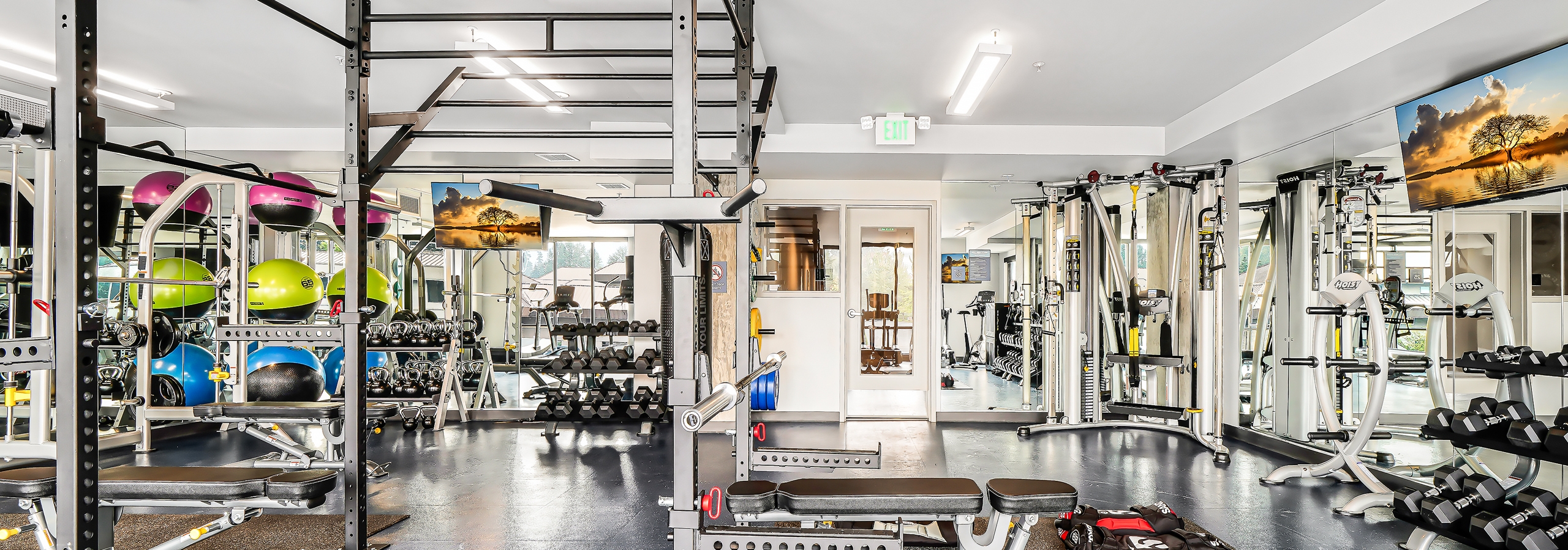 Fitness center at AMLI Spring District apartment building with weight lifting equipment and 2 mirrored walls with mounted TVs