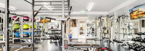 Fitness center at AMLI Spring District apartment building with weight lifting equipment and 2 mirrored walls with mounted TVs