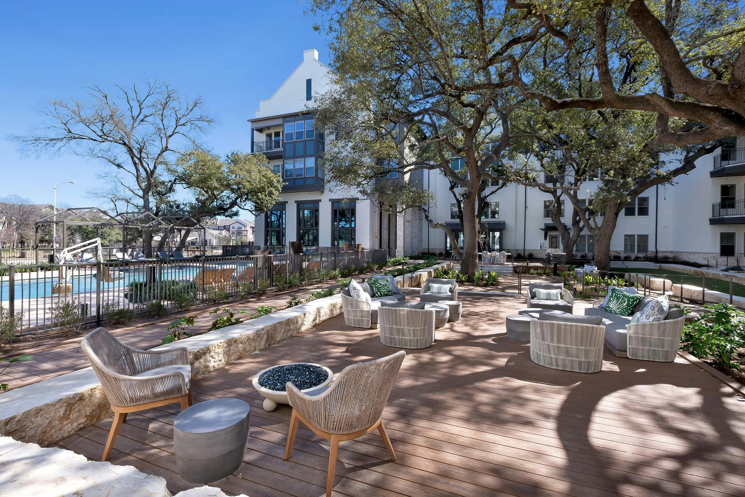 A poolside shaded outdoor lounge at AMLI Lakeline apartments with a circular fire pit and lounge seating with colorful pillows