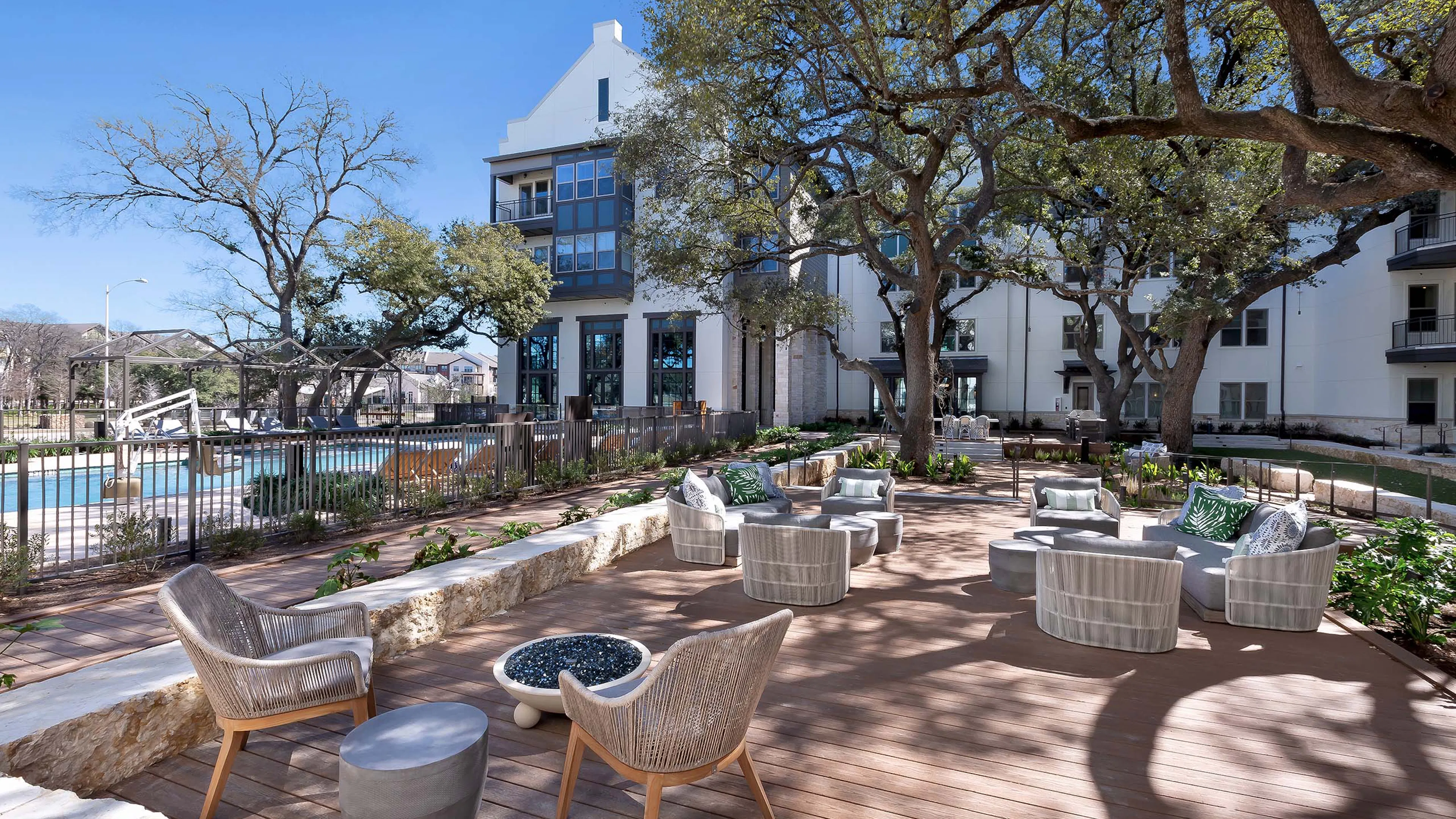 A poolside shaded outdoor lounge at AMLI Lakeline apartments with a circular fire pit and lounge seating with colorful pillows
