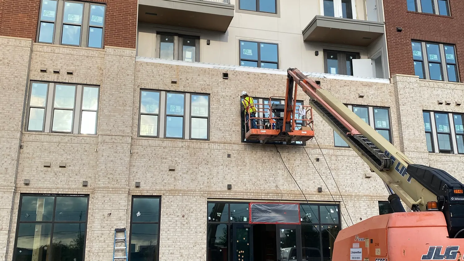 Exterior of AMLI Treehouse apartment building under construction, with workers on an orange crane installing canopies above the leasing office entrance