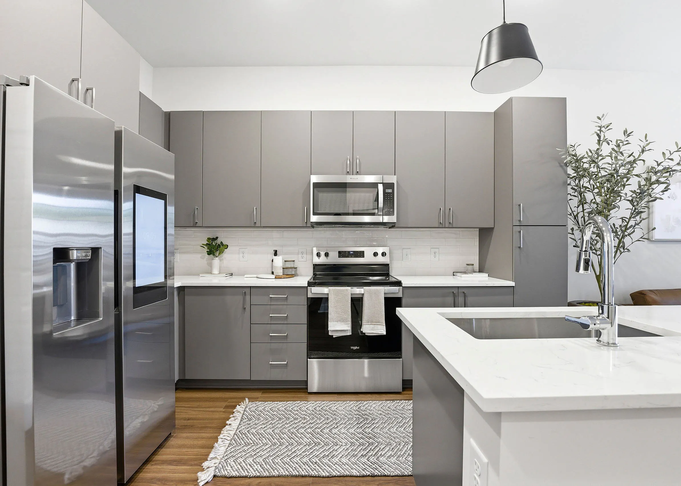 Modern kitchen with gray cabinets, stainless steel appliances, touchscreen refrigerator, white countertops and white island with a sink