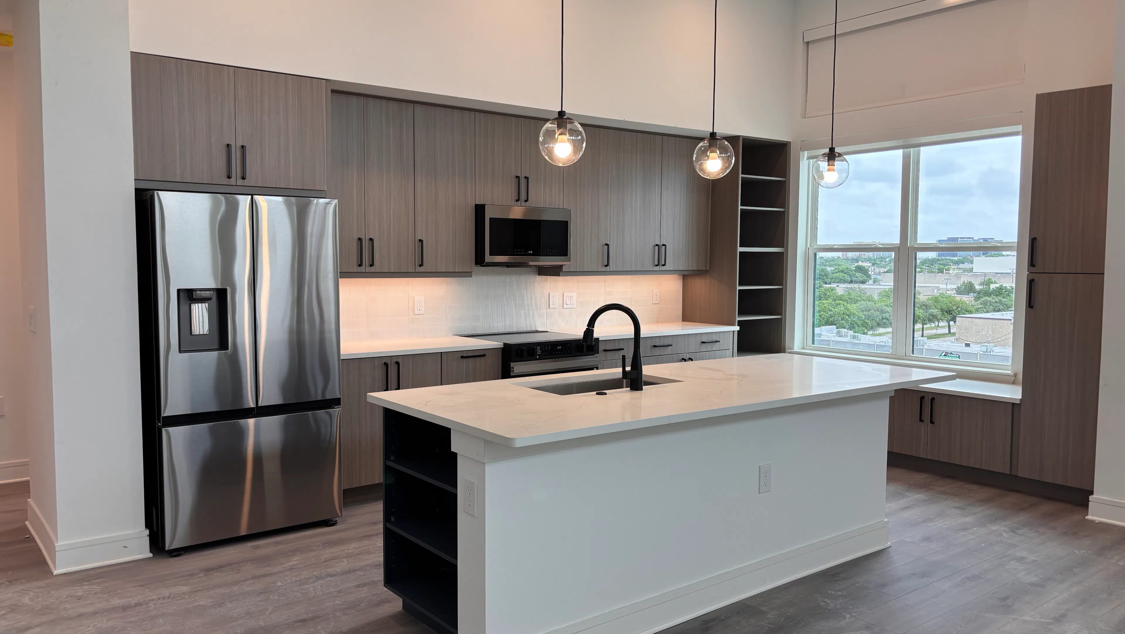 Modern kitchen with island, pendant lights, stainless steel fridge, gray cabinets, white countertops, and large window at AMLI Treehouse