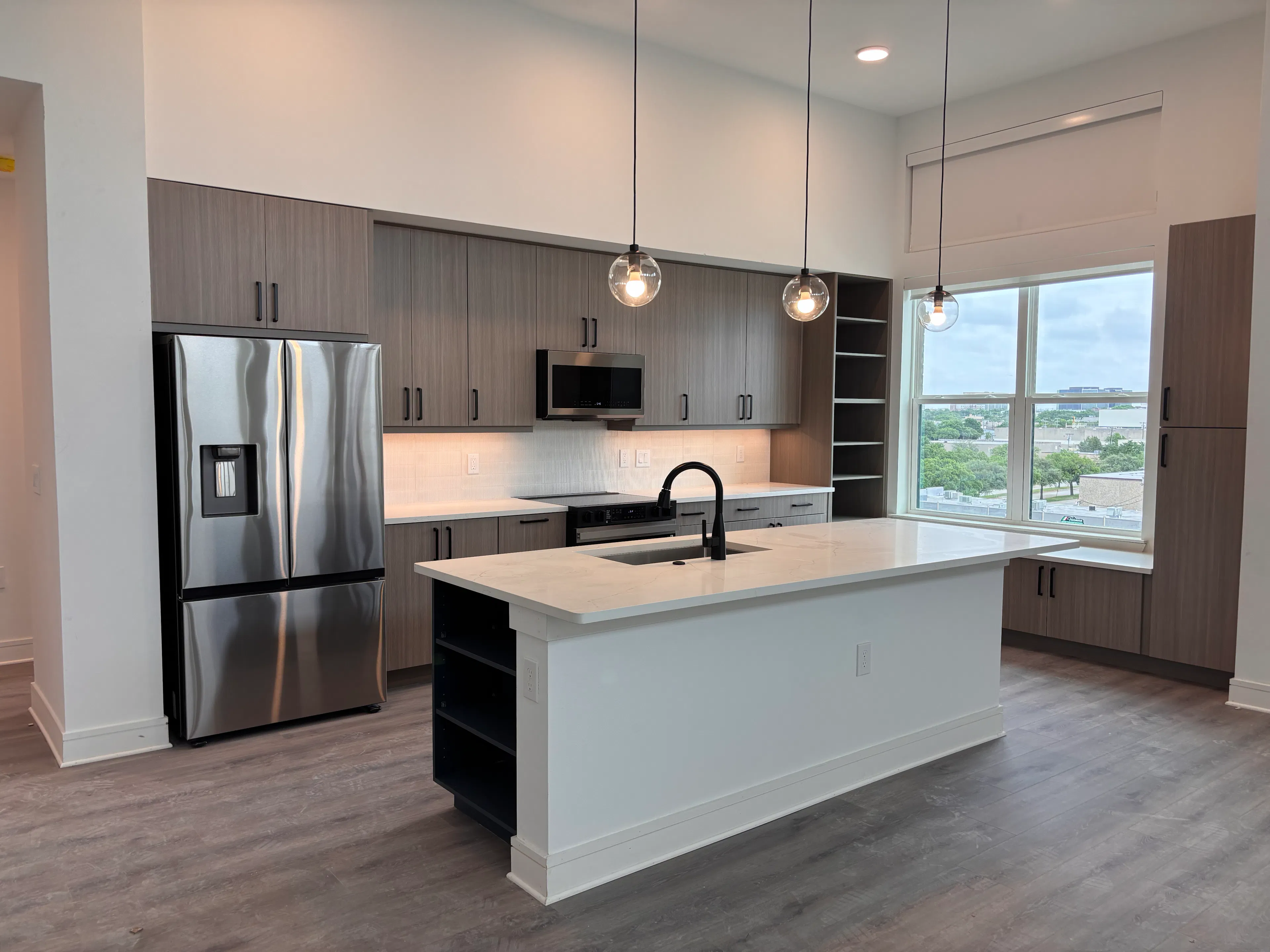Modern kitchen with island, pendant lights, stainless steel fridge, gray cabinets, white countertops, and large window at AMLI Treehouse