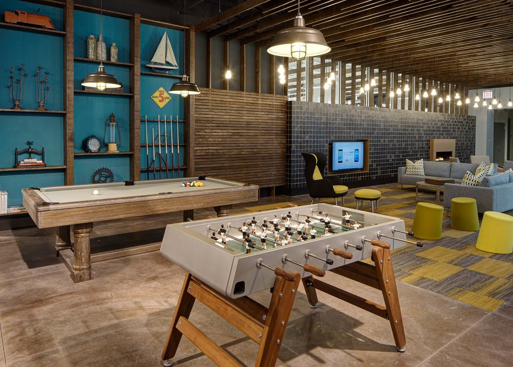 Modern clubroom at AMLI Lofts with billiard and foosball tables and a seating area with a large TV in the background