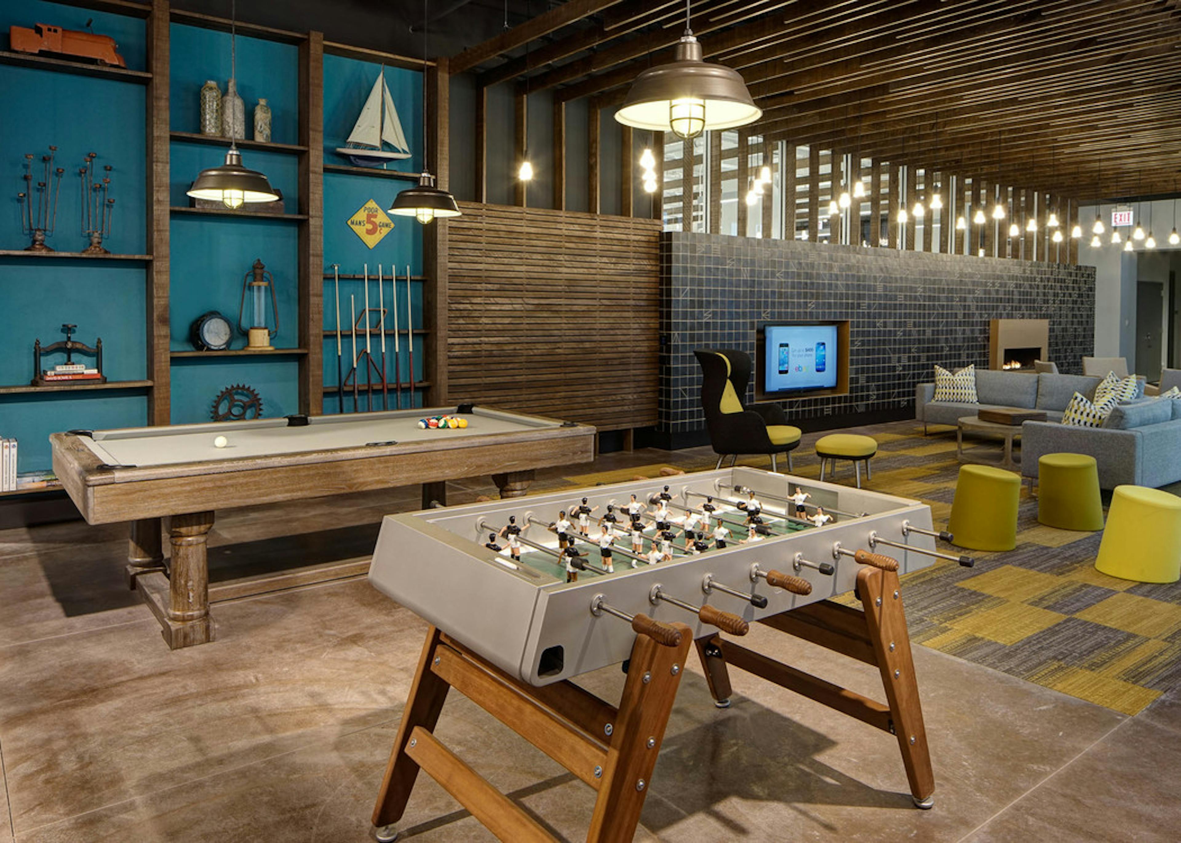 Modern clubroom at AMLI Lofts with billiard and foosball tables and a seating area with a large TV in the background