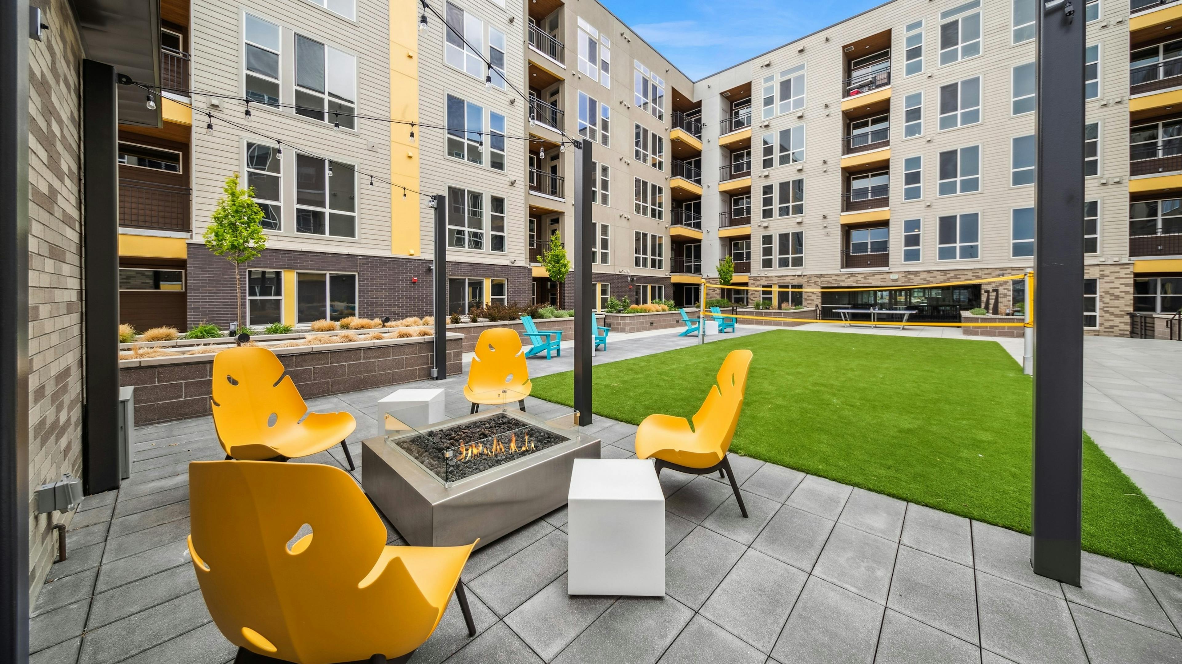 AMLI RiNo courtyard with a firepit surrounded by 4 yellow chairs with string lights above adjacent to a turf badminton court  