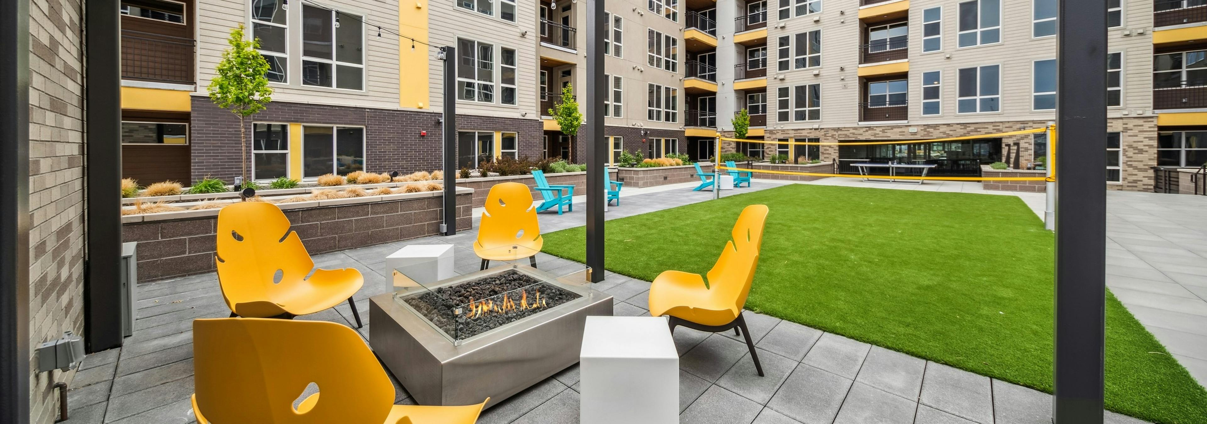 AMLI RiNo courtyard with a firepit surrounded by 4 yellow chairs with string lights above adjacent to a turf badminton court  