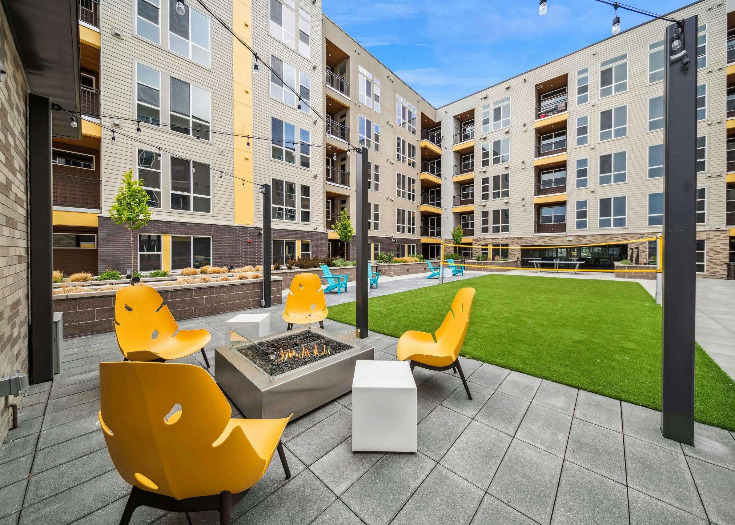 AMLI RiNo courtyard with a firepit surrounded by 4 yellow chairs with string lights above adjacent to a turf badminton court