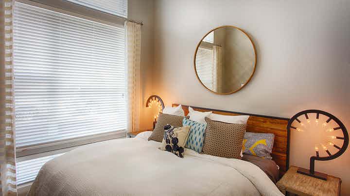 A bedroom at AMLI Denargo Market apartments featuring a bed with a wooden head board and a circular mirror and large window