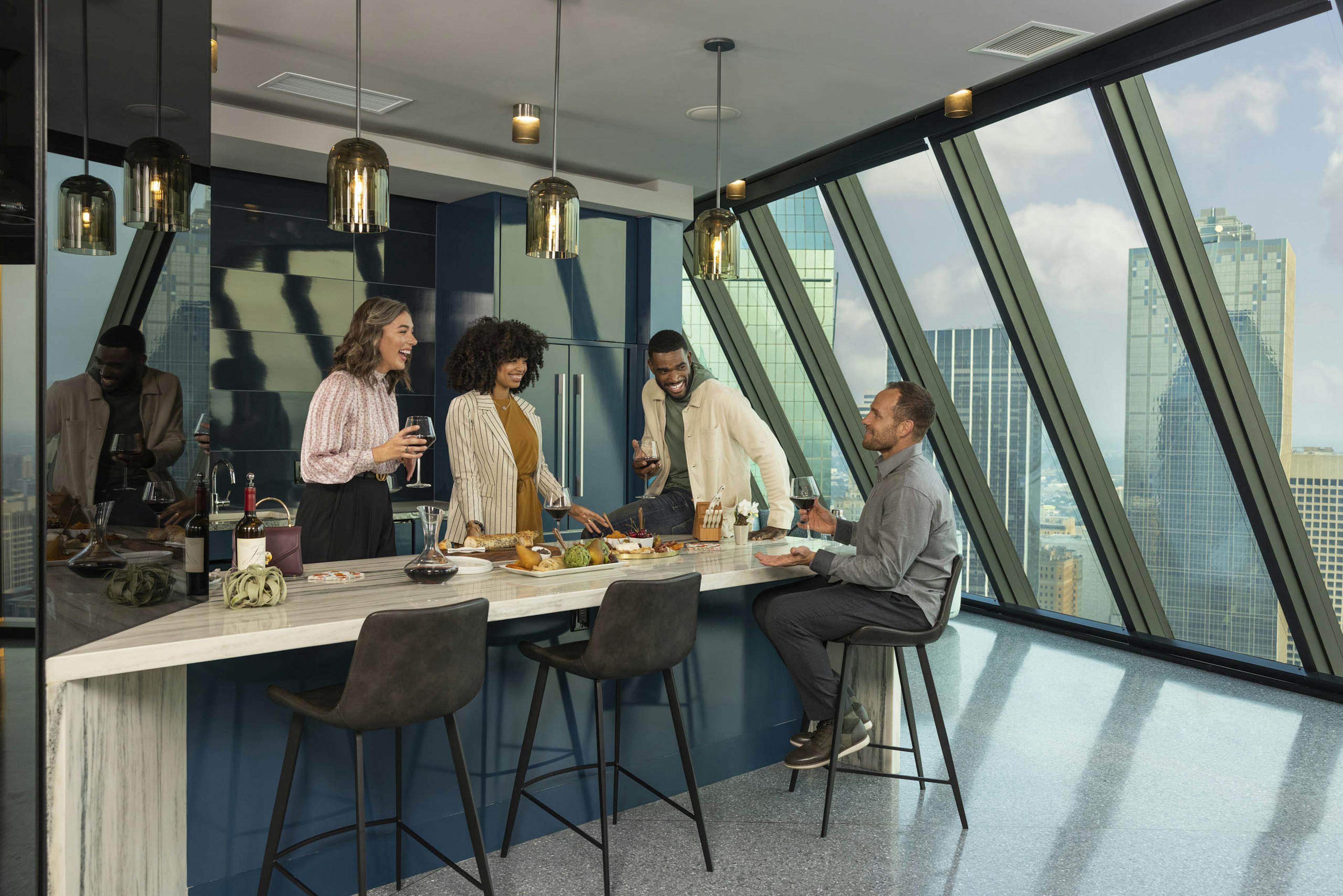 Two couples enjoying wine around a kitchen island at AMLI Fountain Place apartments with views of downtown Dallas 