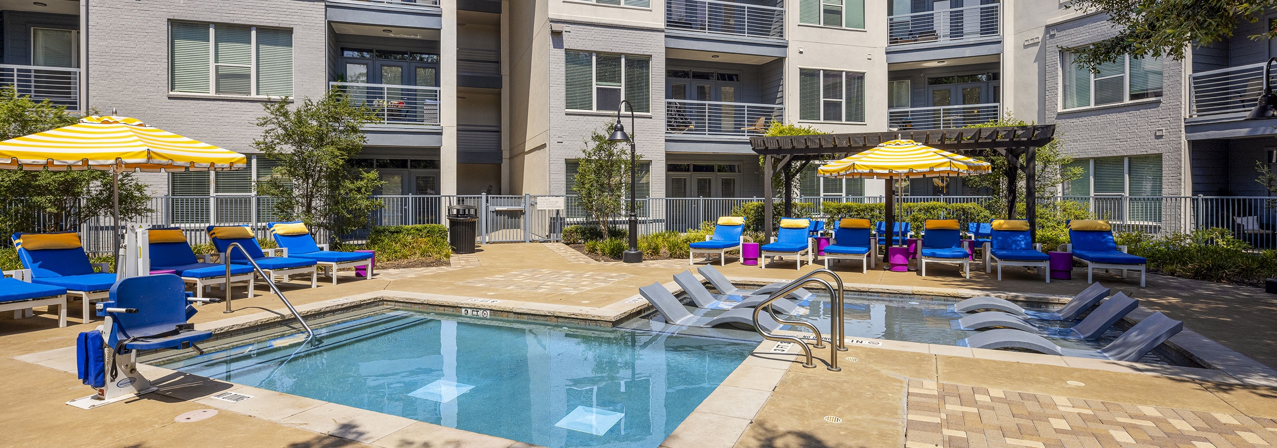 AMLI South Shore apartment pool with blue lounge chairs and yellow and white umbrellas in front of gray building