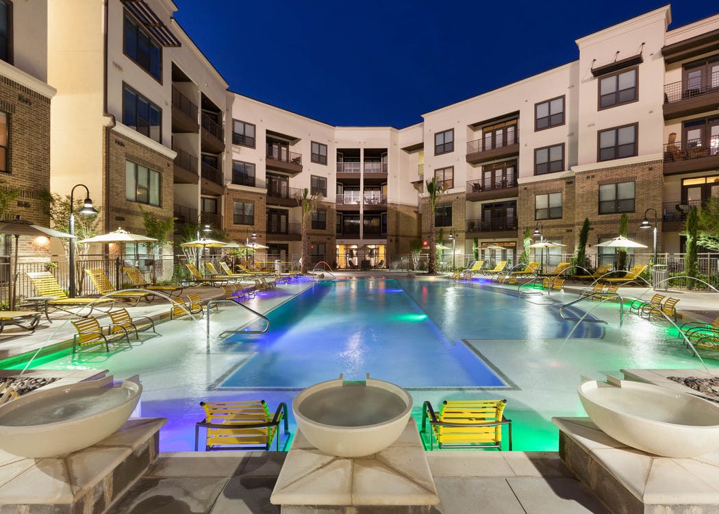 Nighttime view of swimming pool with yellow lounge furniture and fountains at AMLI at the Ballpark apartment building