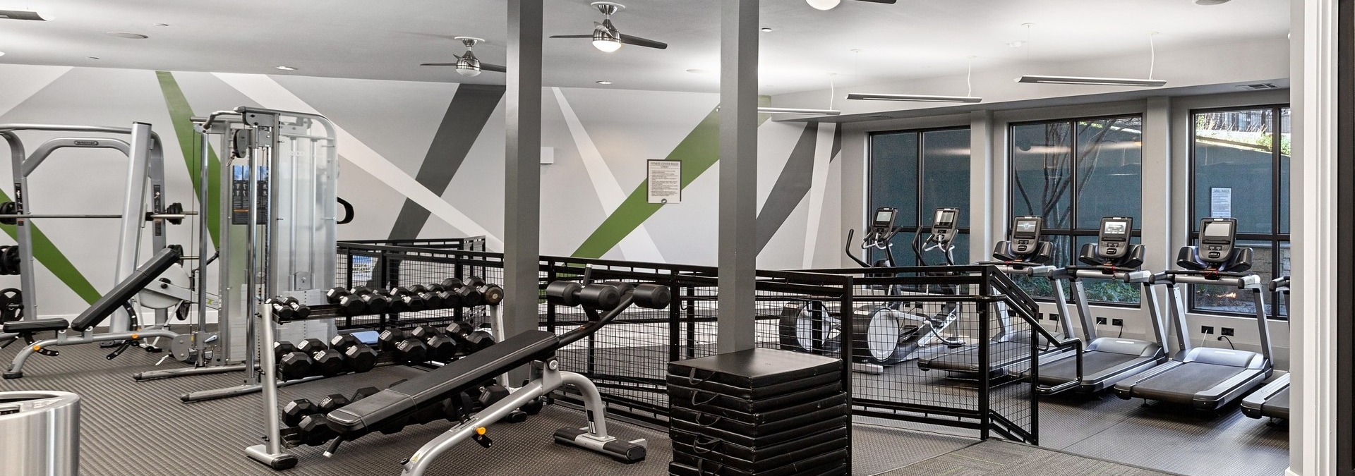 AMLI Parkside fitness center with a green and white striped accent wall behind free weights and machines and treadmills