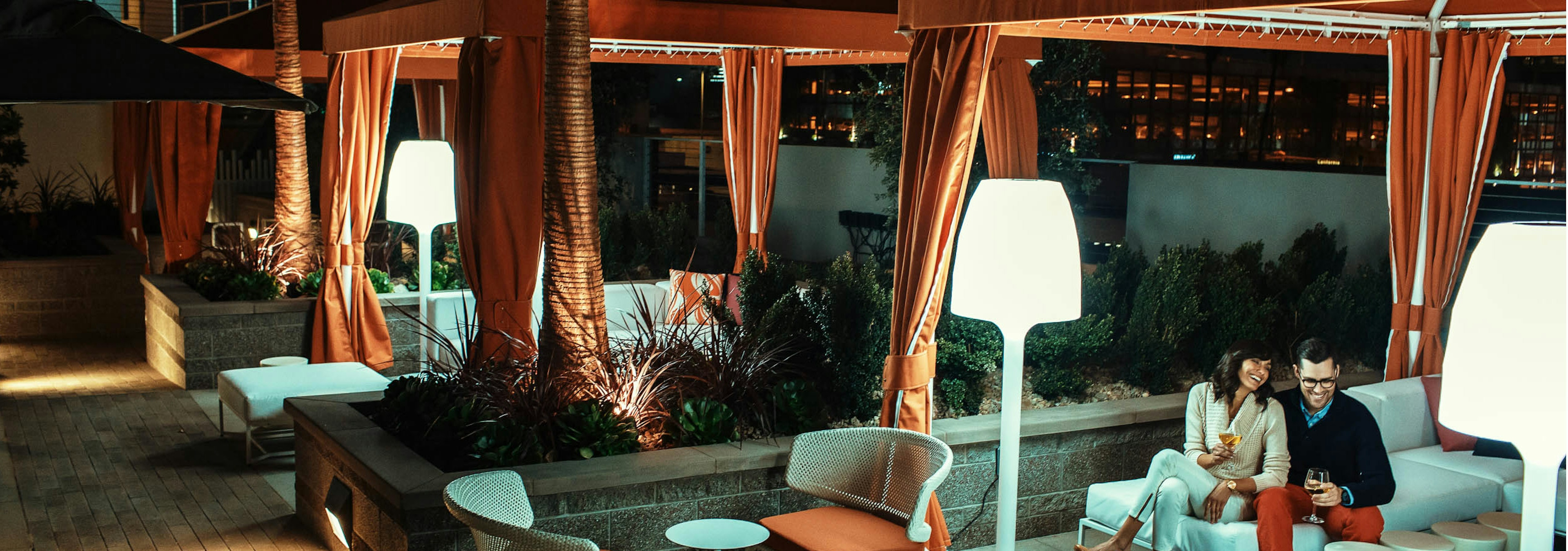 Nighttime view of AMLI Lex on Orange pool deck personal curtained cabanas with comfortable seating, patio lamps and a couple 