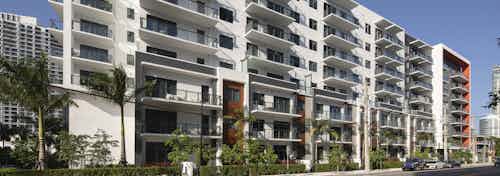 Daytime view of AMLI Midtown Miami apartment building with a white façade with orange highlights set on tree lined street