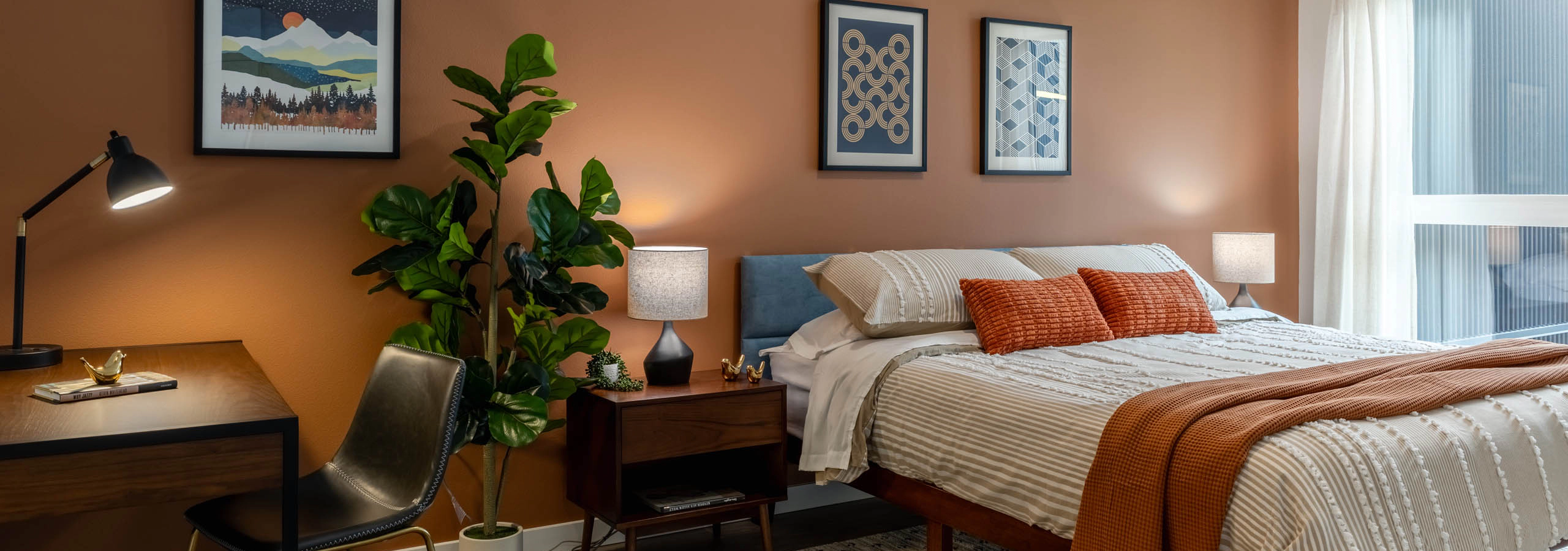 Large bedroom with orange walls, bed with wooden nightstand, and small wooden desk in the corner.