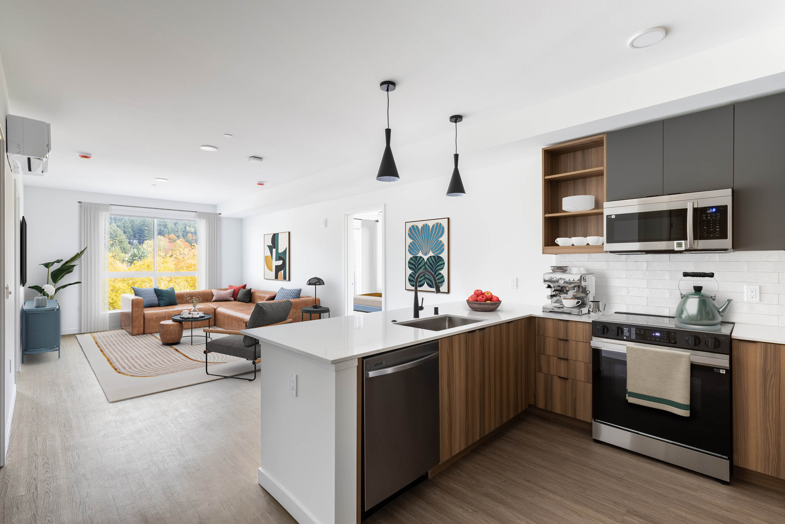 Open view of AMLI Redmond Way apartment kitchen and living space with white pendant lighting, wood floors, and natural window light.