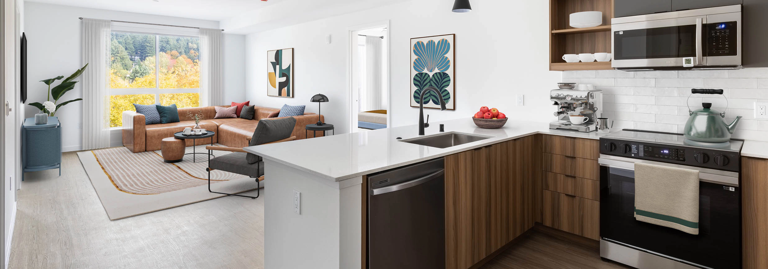 Open view of AMLI Redmond Way apartment kitchen and living space with white pendant lighting, wood floors, and natural window light.