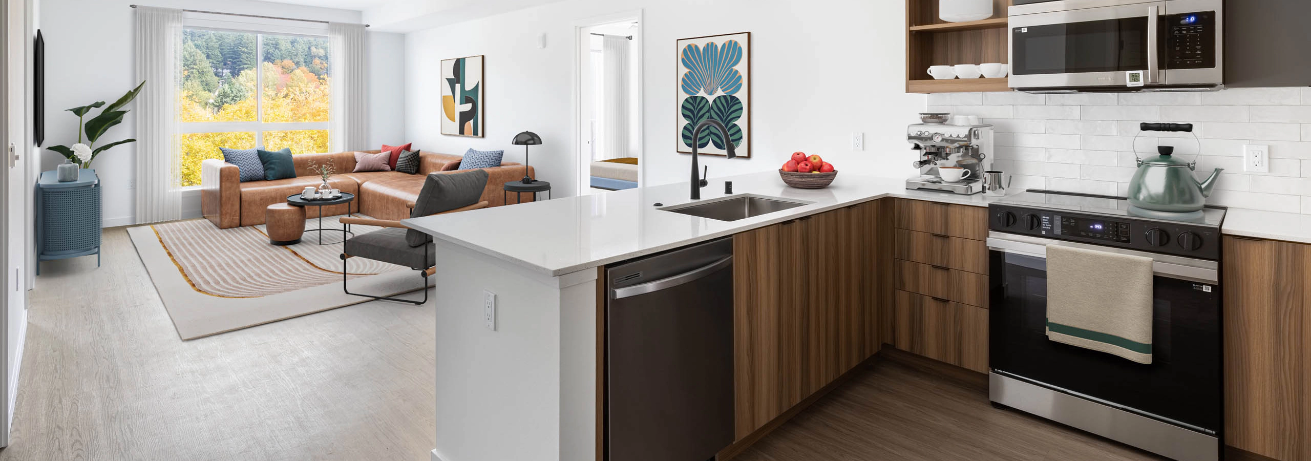 Open view of AMLI Redmond Way apartment kitchen and living space with white pendant lighting, wood floors, and natural window light.