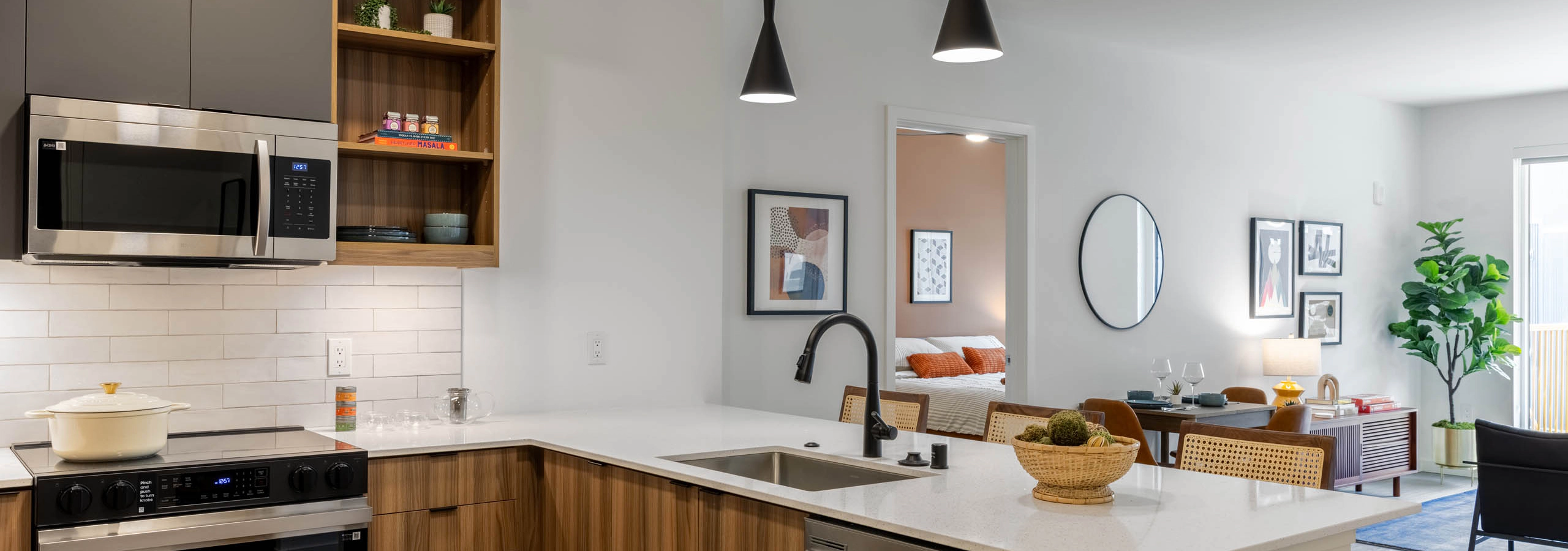Kitchen area with stainless-steel appliances, wooden cabinetry and plank flooring connected to the living area.