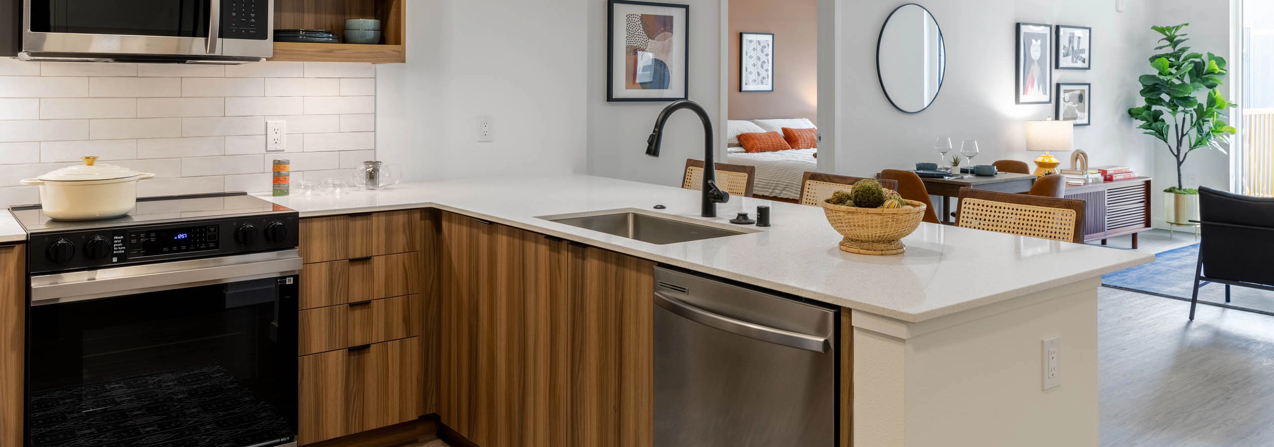 Kitchen area with stainless-steel appliances, wooden cabinetry and plank flooring connected to the living area.