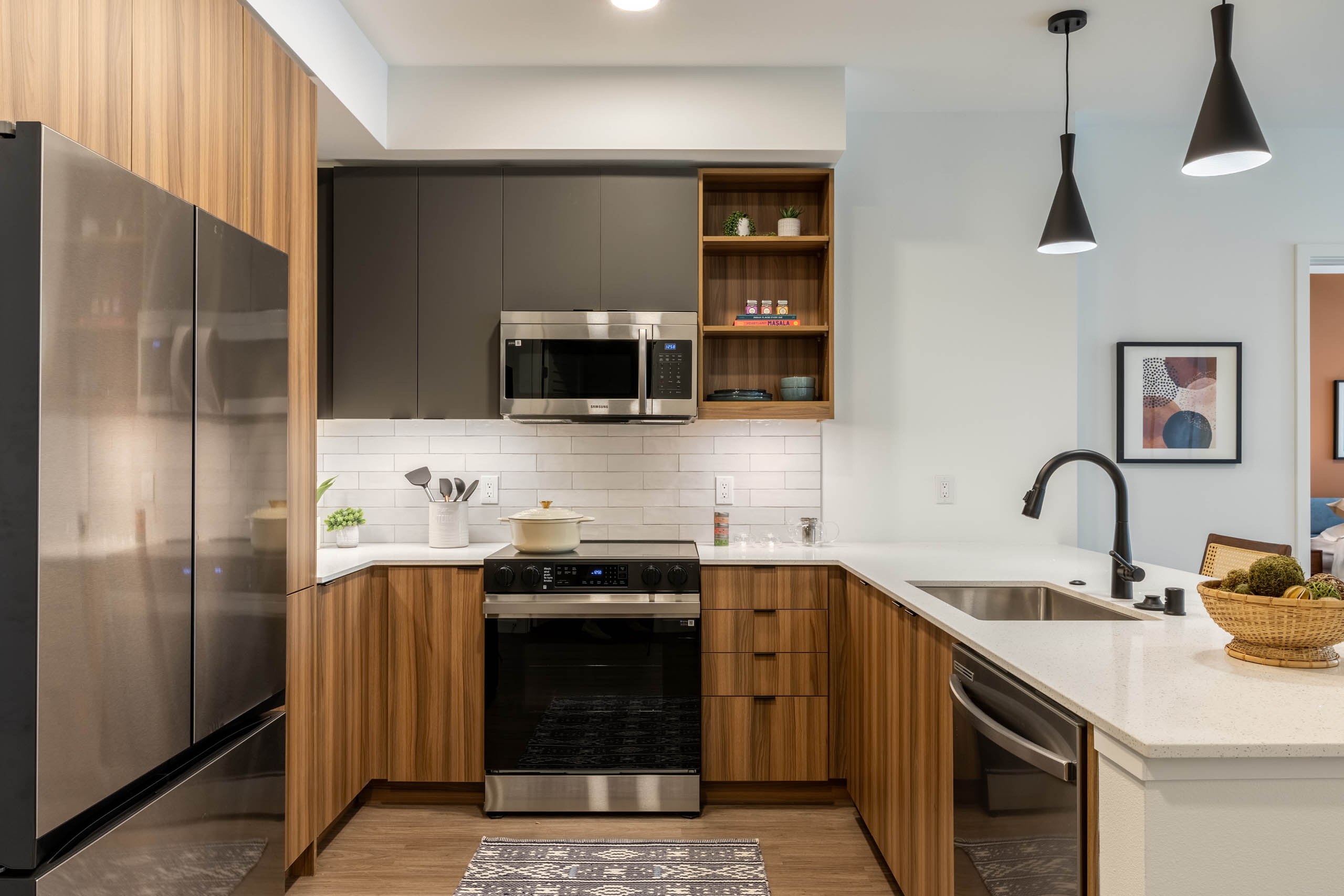 Kitchen area with stainless-steel appliances, wooden brown and grey cabinetry and plank flooring.