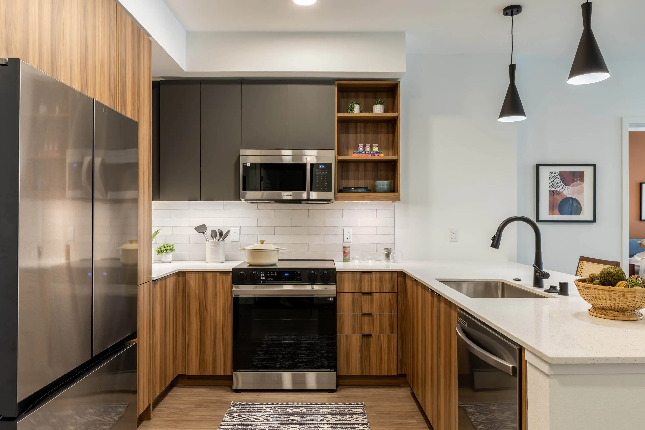 Kitchen area with stainless-steel appliances, wooden brown and grey cabinetry and plank flooring.