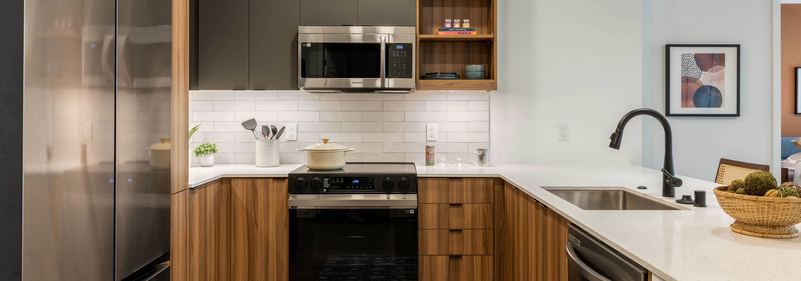 Kitchen area with stainless-steel appliances, wooden brown and grey cabinetry and plank flooring.