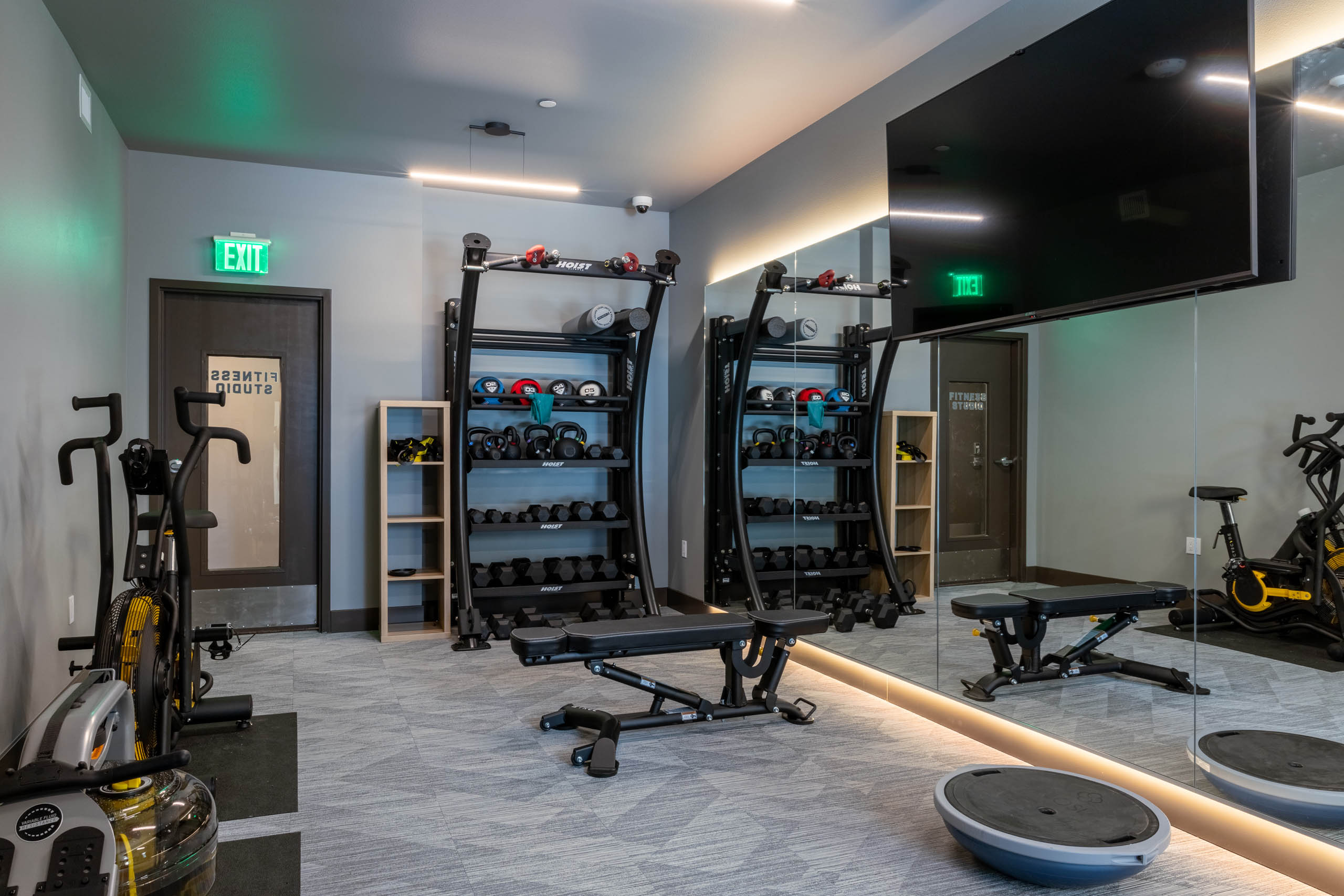 Fully equipped fitness studio with free weights, and cardio equipment with a full- length mirror and a mounted TV.