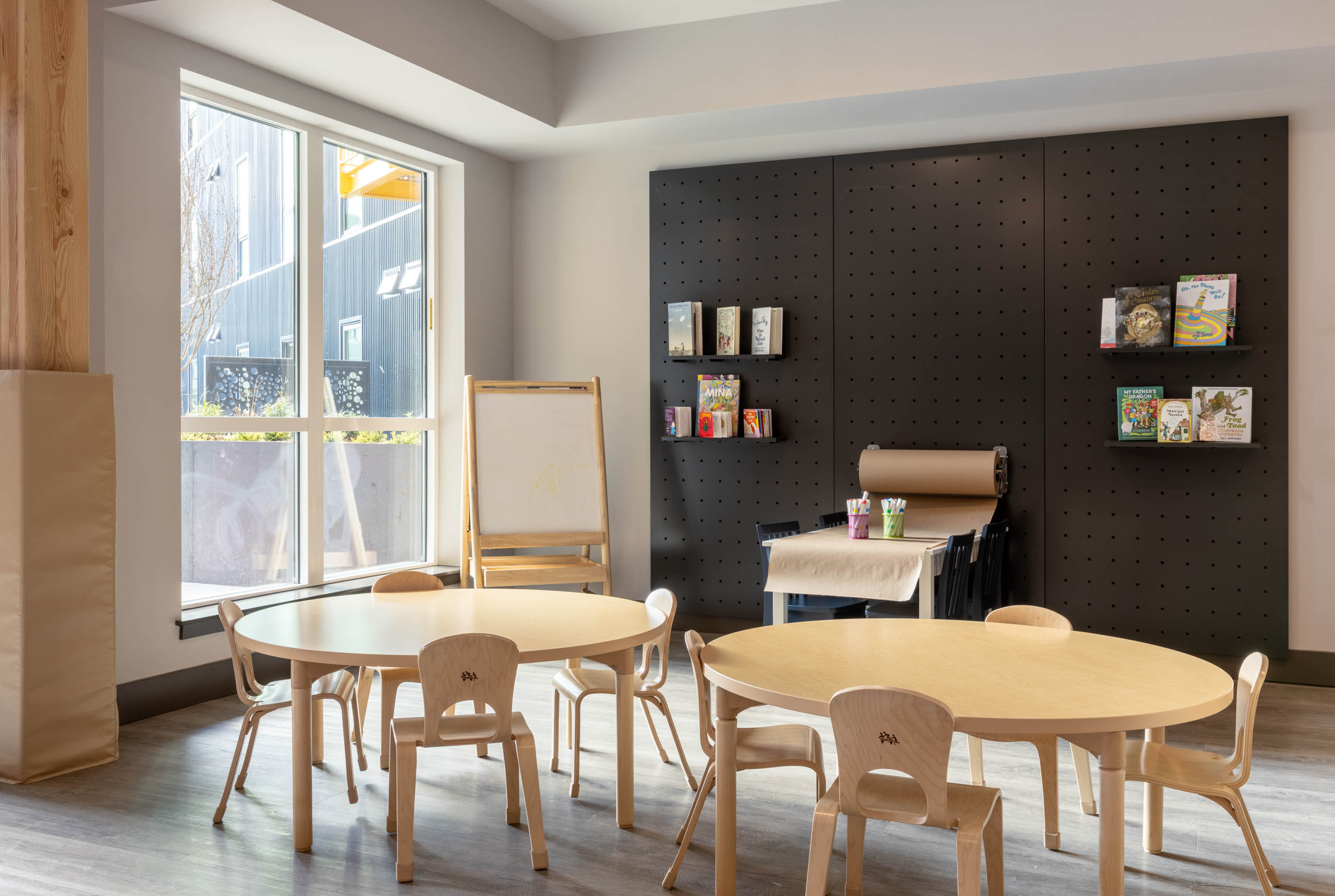 Bright play area with wooden seating for children, featuring a wall with books and a whiteboard in the corner.