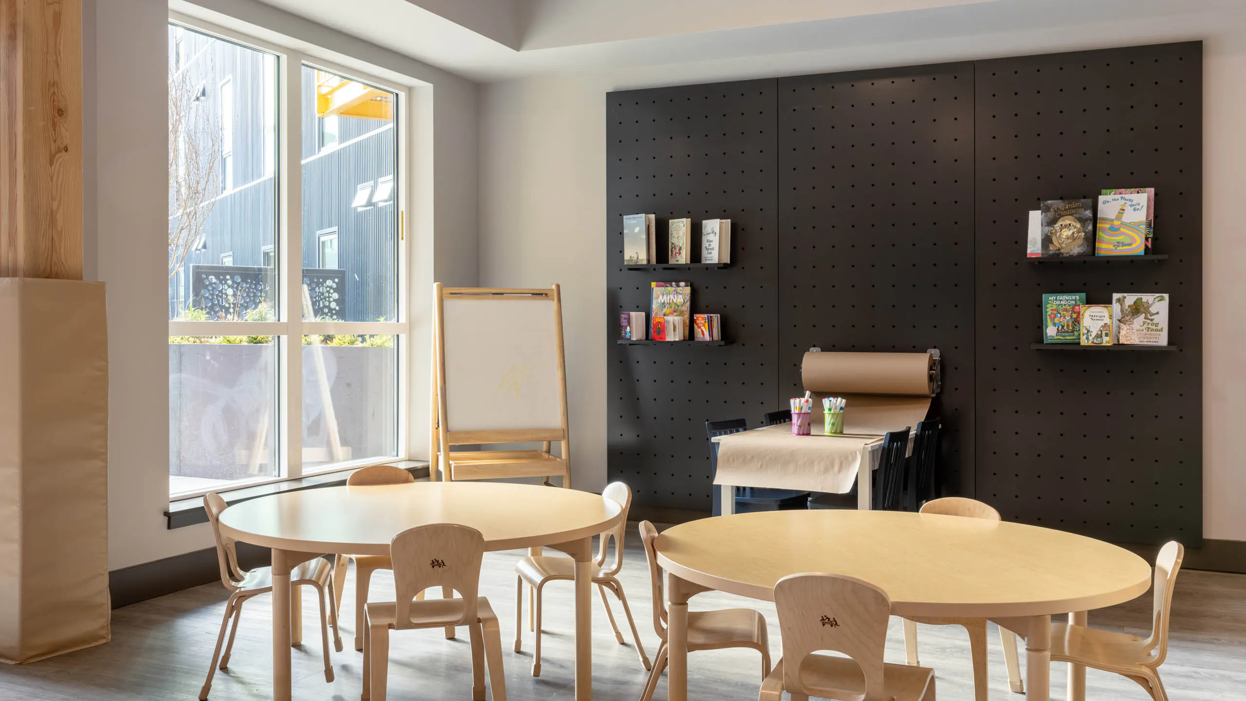 Bright play area with wooden seating for children, featuring a wall with books and a whiteboard in the corner.