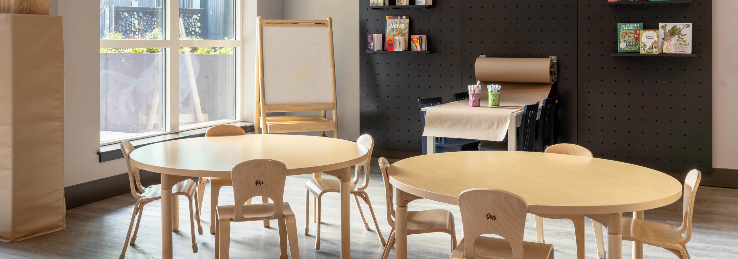 Bright play area with wooden seating for children, featuring a wall with books and a whiteboard in the corner.