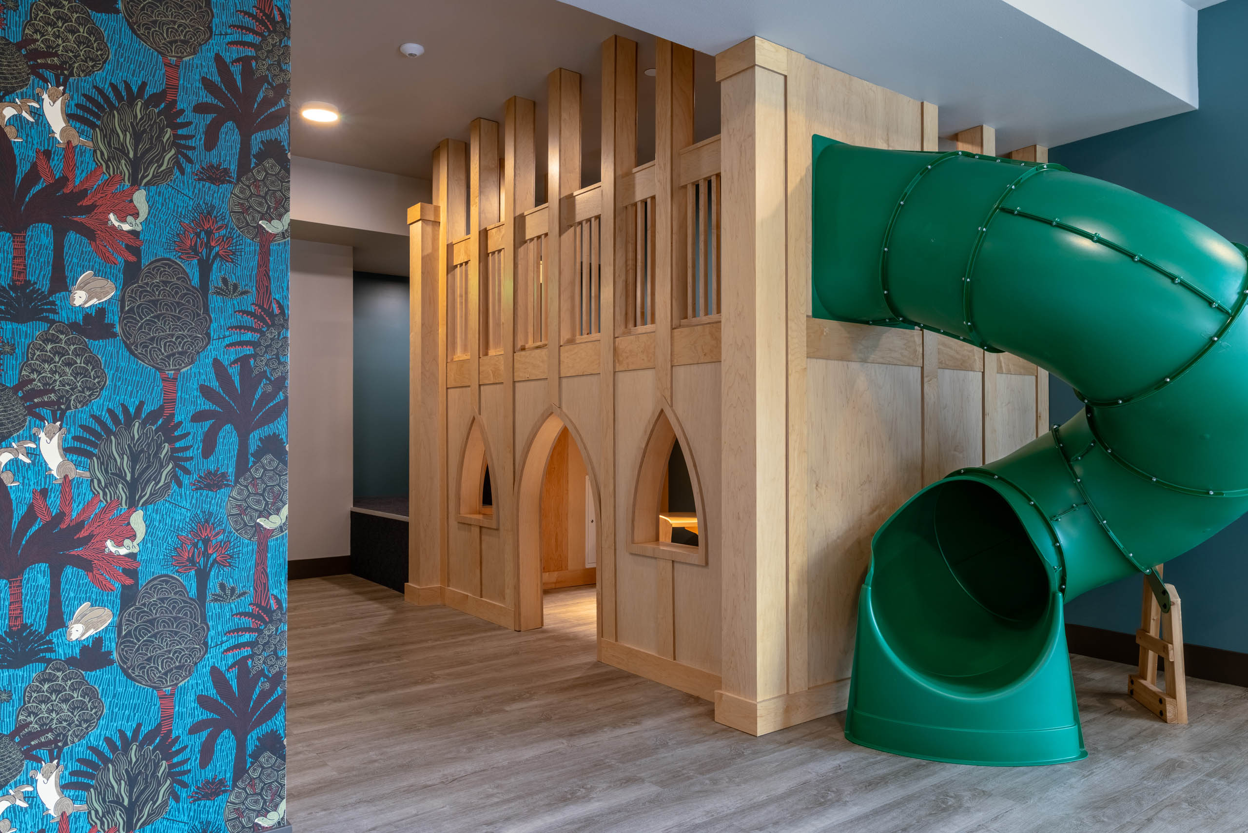 Children’s play area with a green slide and wooden playhouse with colorful patterned walls.