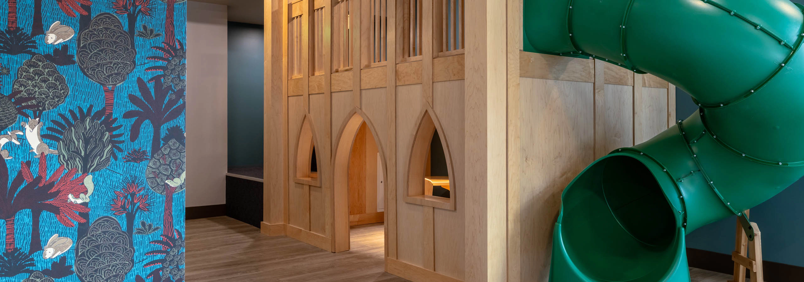 Children’s play area with a green slide and wooden playhouse with colorful patterned walls.