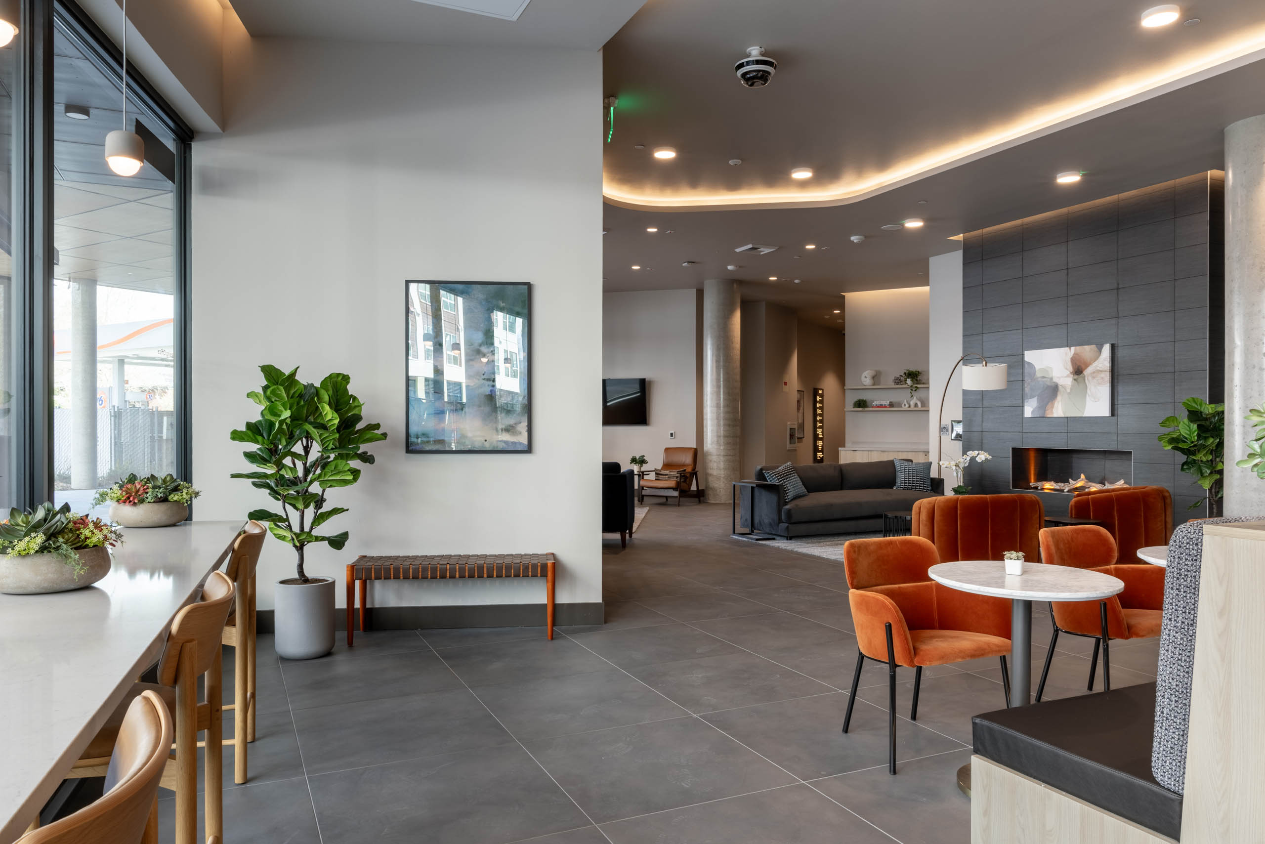 Community clubroom with multiple social and work-from-home spaces, featuring a large gray fireplace and gray furniture nearby.