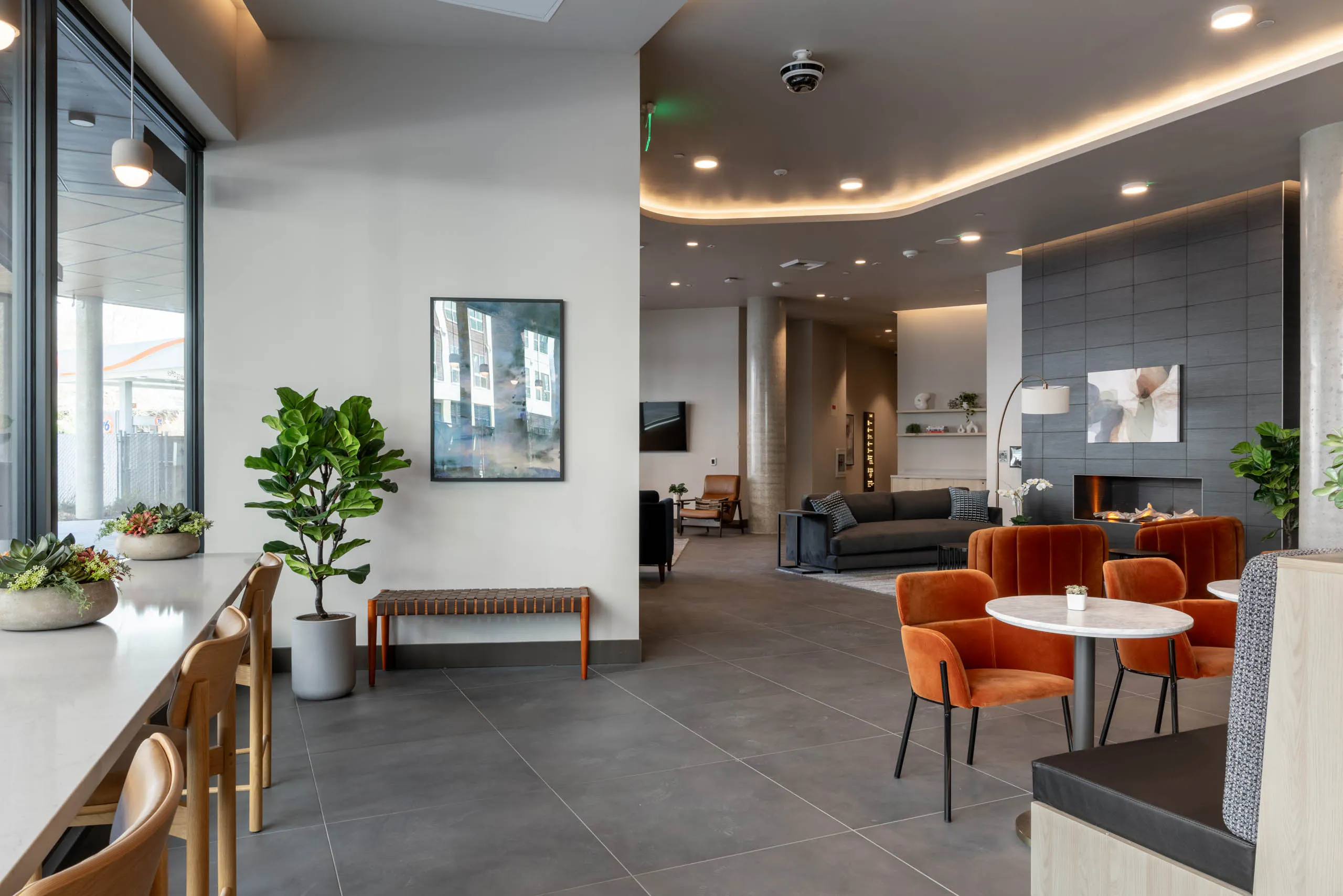 Community clubroom with multiple social and work-from-home spaces, featuring a large gray fireplace and gray furniture nearby.