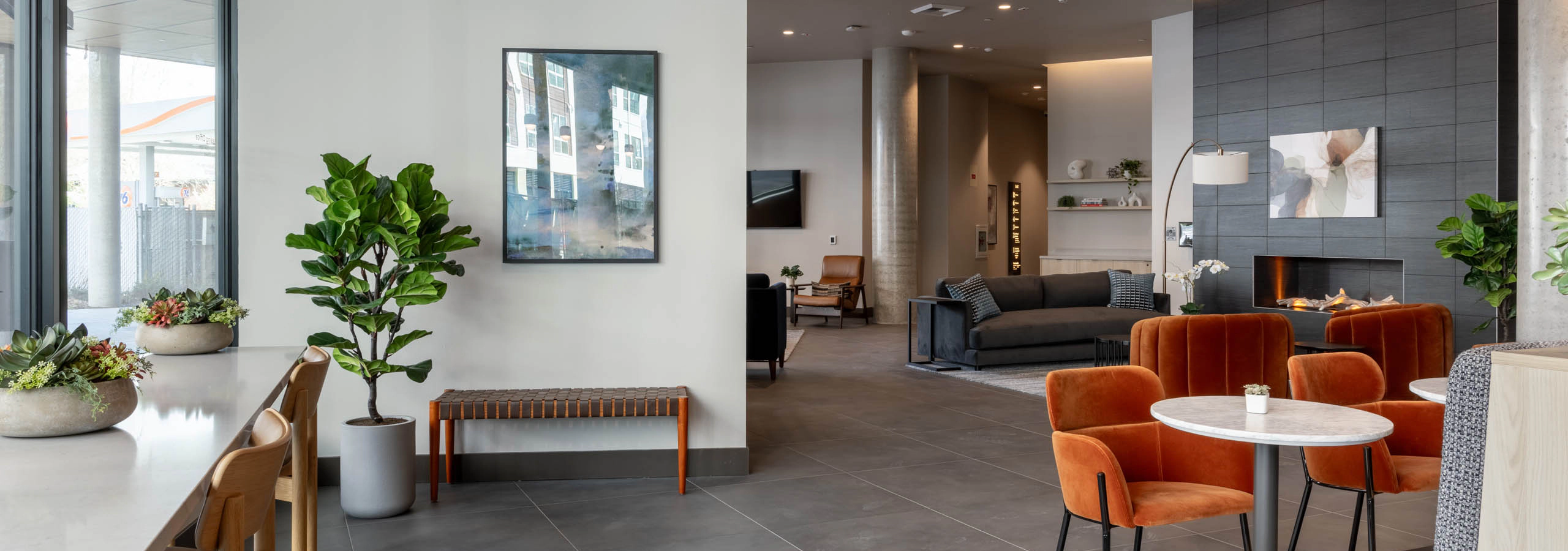 Community clubroom with multiple social and work-from-home spaces, featuring a large gray fireplace and gray furniture nearby.