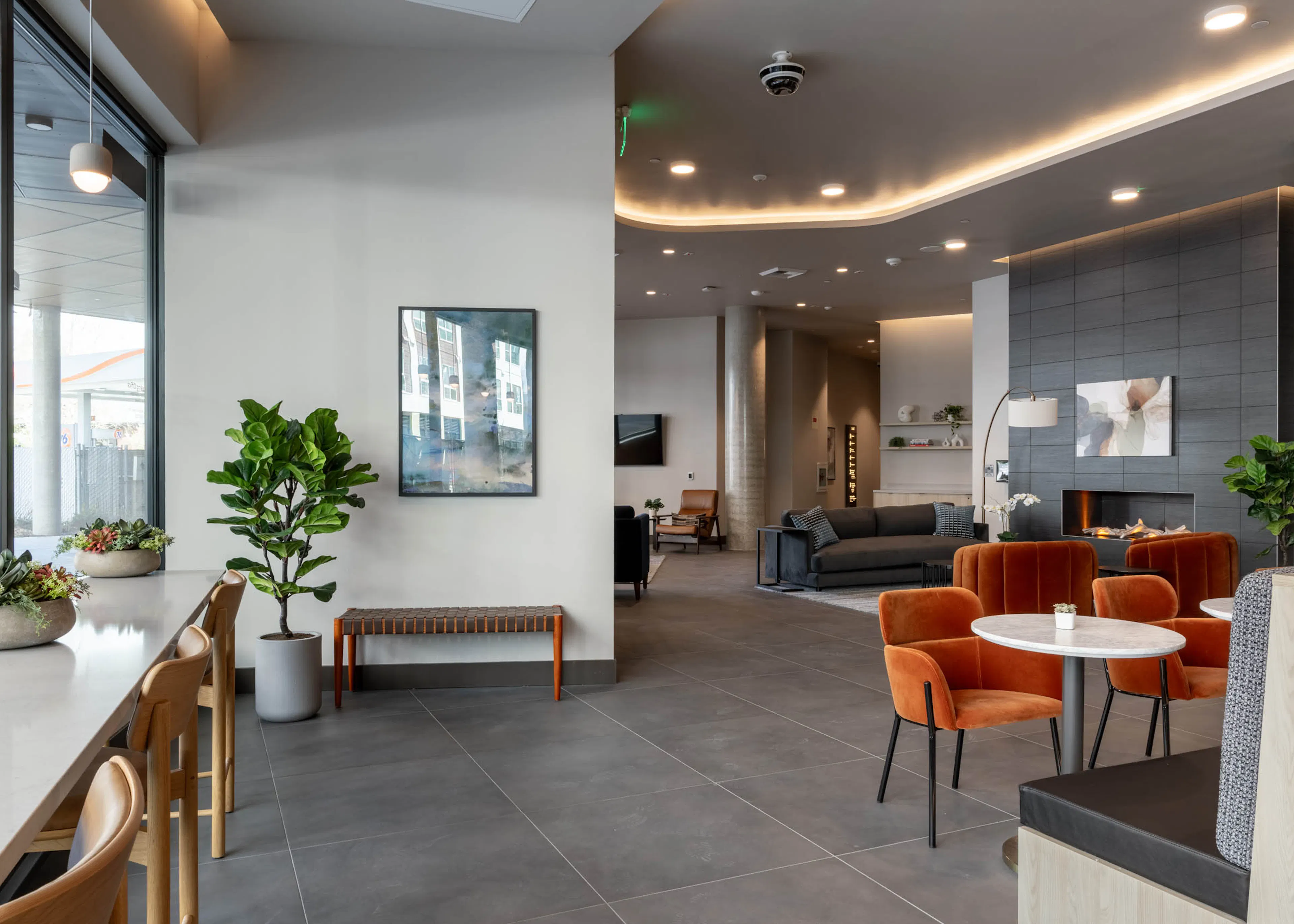 Community clubroom with multiple social and work-from-home spaces, featuring a large gray fireplace and gray furniture nearby.